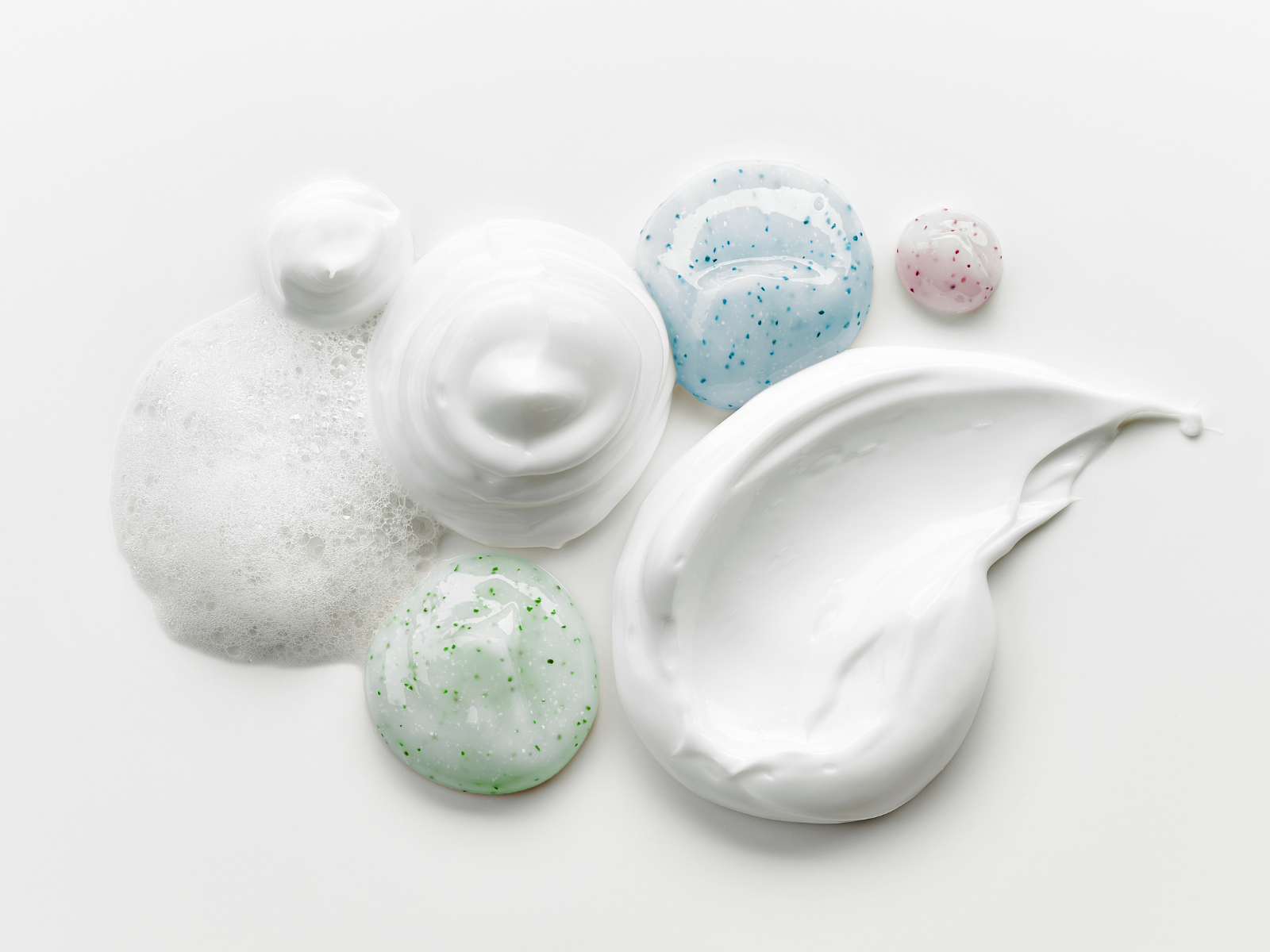 over view of different face care ointments and creams droplets and smudges on white backdrop