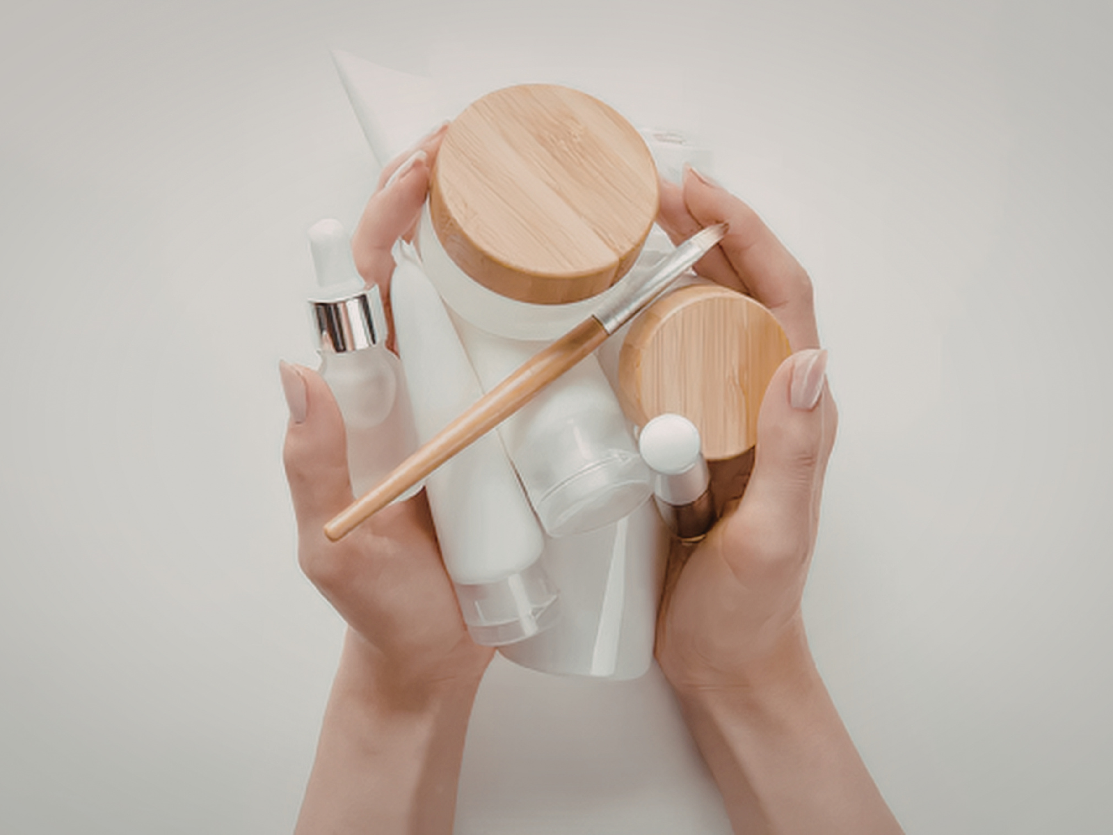 Women hold unlabled beauty bottles, tubs, and dropper bottles.
