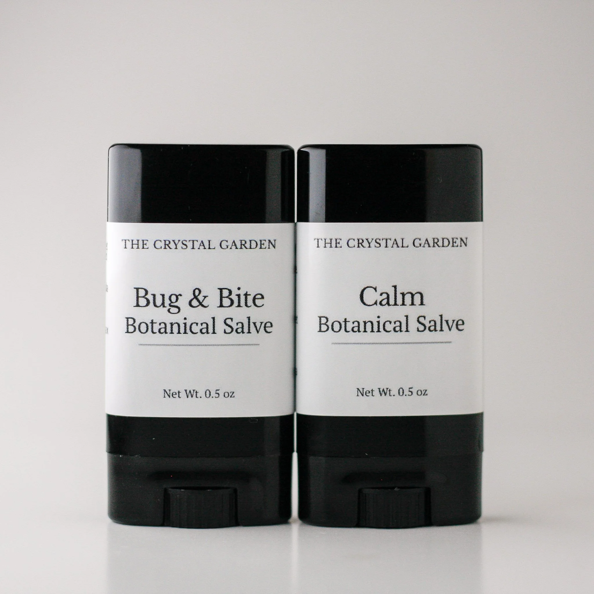 Two botanical salve tubes from The Crystal Garden displayed side by side on a neutral background