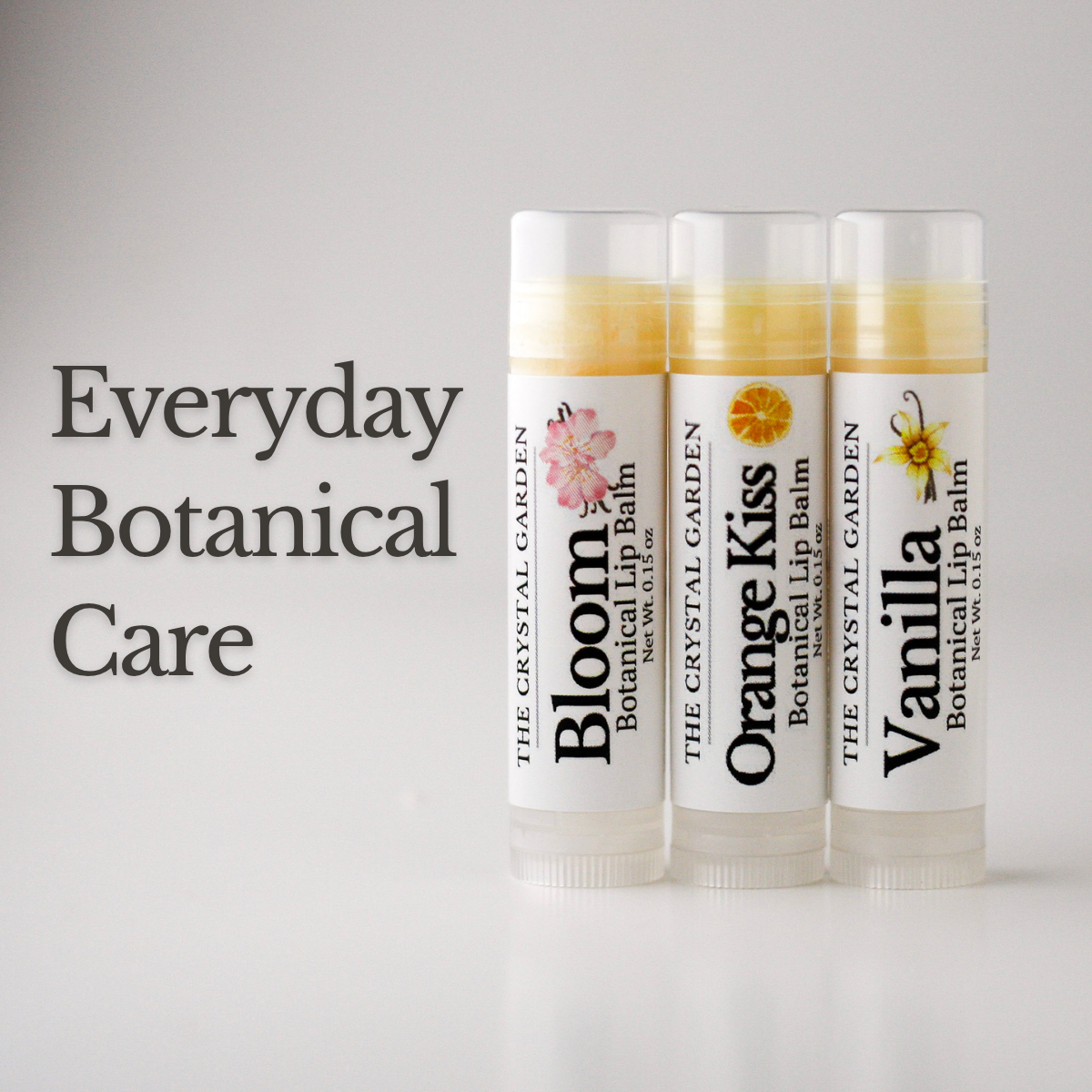 Three botanical lip balms in white tubes on a white to light gray background, Botanical Lip Balm 3-pack by The Crystal Garden.