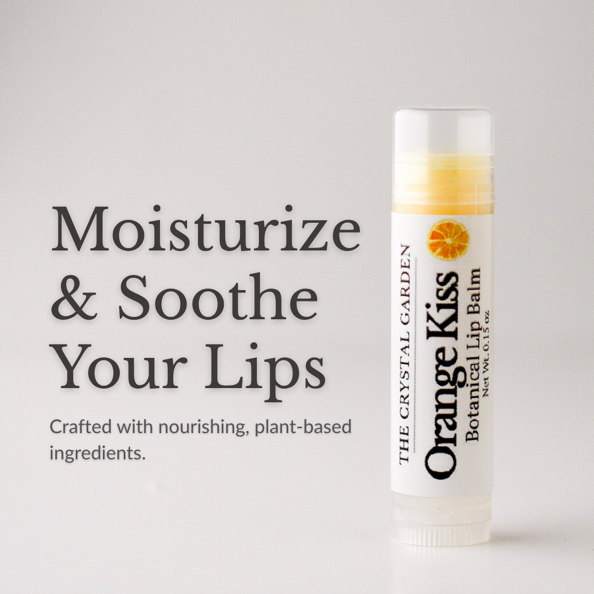 Orange Kiss natural lip balm in white tube with botanical label on a white to light gray background, plant-based lip care by The Crystal Garden.