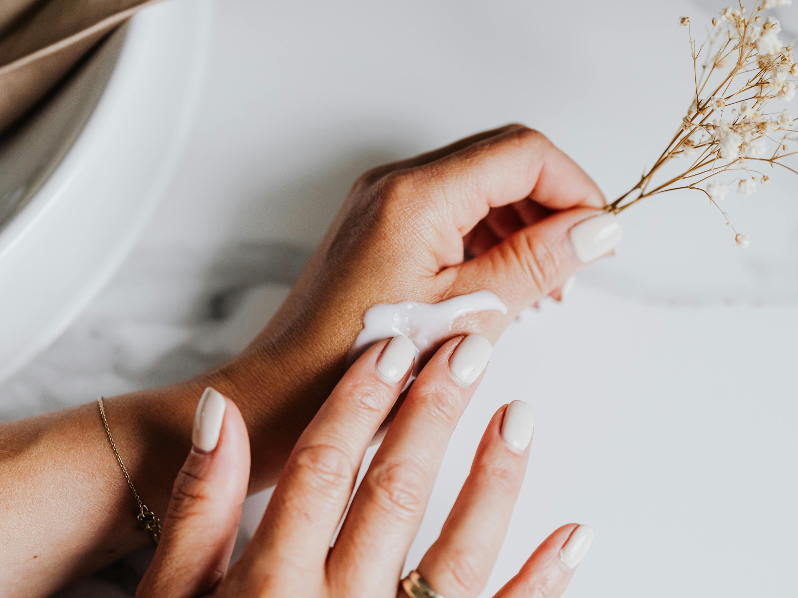 close up of hands apply white lotion holding dried flowers