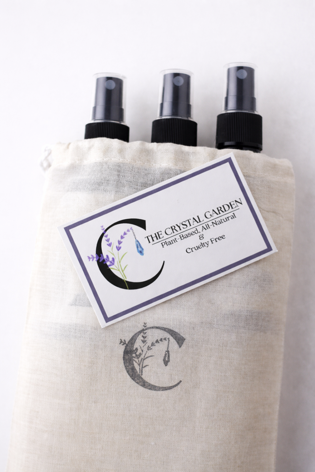 Muslin gift bag with The Crystal Garden logo holding three spray bottles with branded card on neutral background