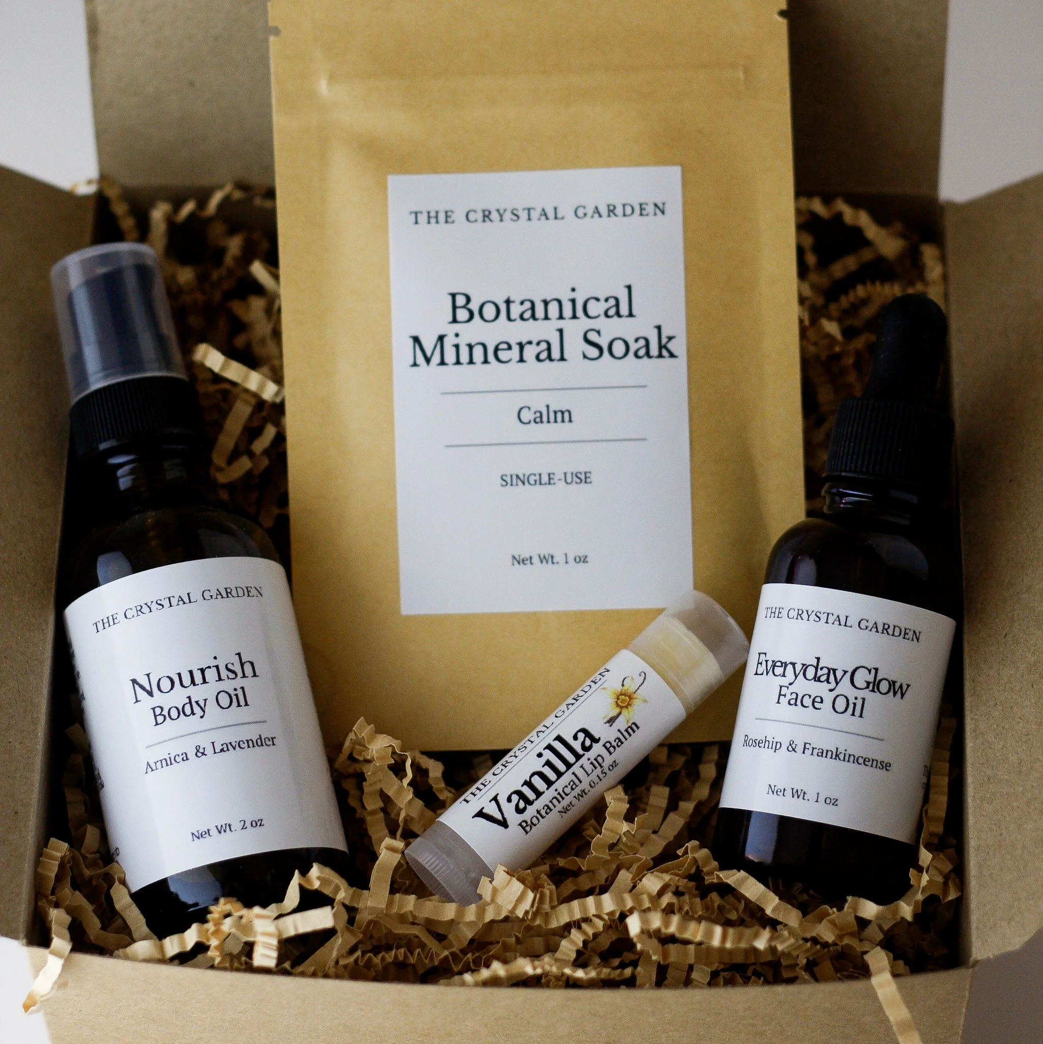 Plant-based self care gift set with body oil, face oil, botanical mineral soak, and lip balm on a neutral background