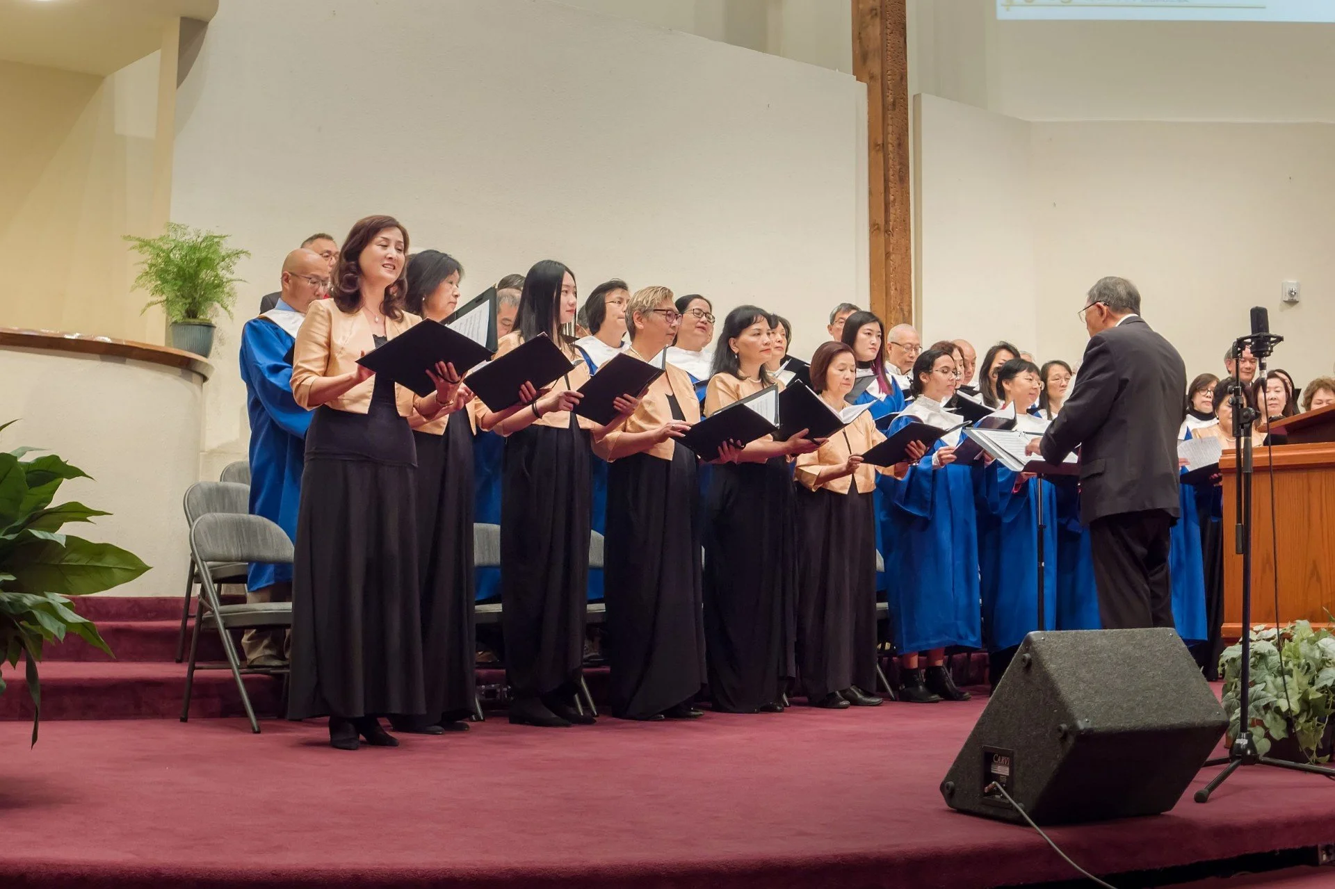 Chorus group singing guided by a conductor on stage in a church or concert hall.