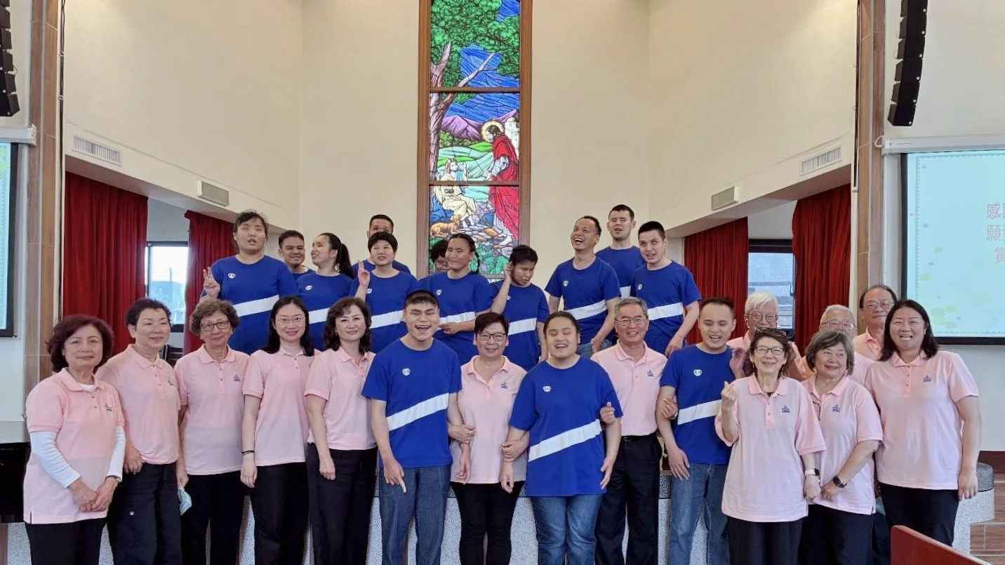 Group photo of volunteers and staff inside a church, with a stained glass window depicting a biblical scene in the background.