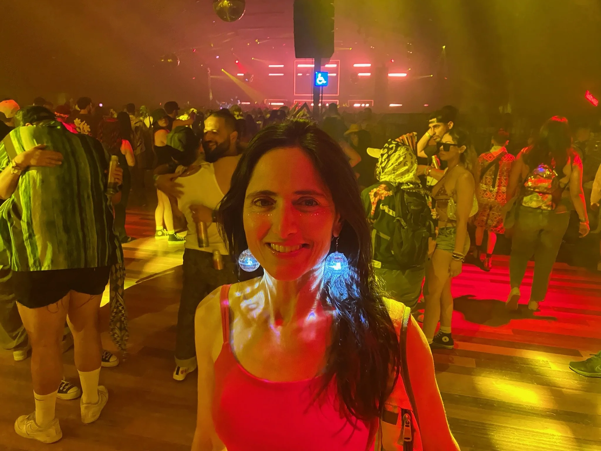 A person with short hair is in a dark room illuminated by pink and purple lights, standing against a patterned wall.