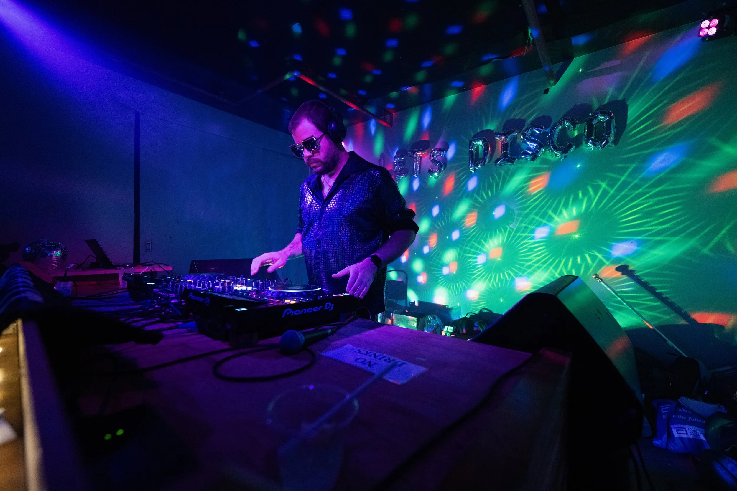 A silhouette of a person performing as a DJ on stage, illuminated by blue spotlight and surrounded by dark ambient lighting and fog.