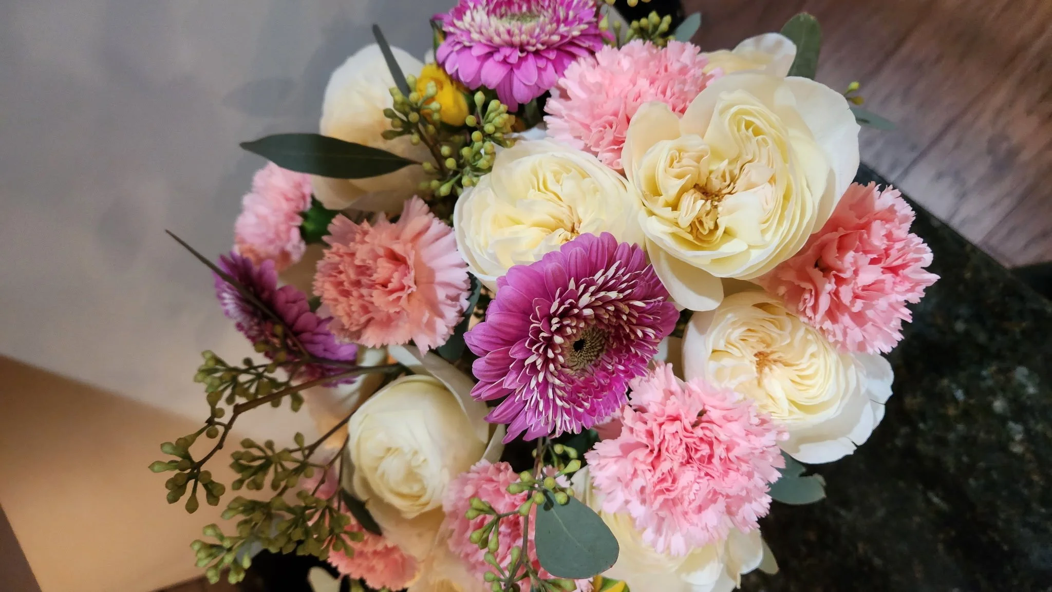A bouquet of pink carnations, white roses, purple daisies, and greenery.