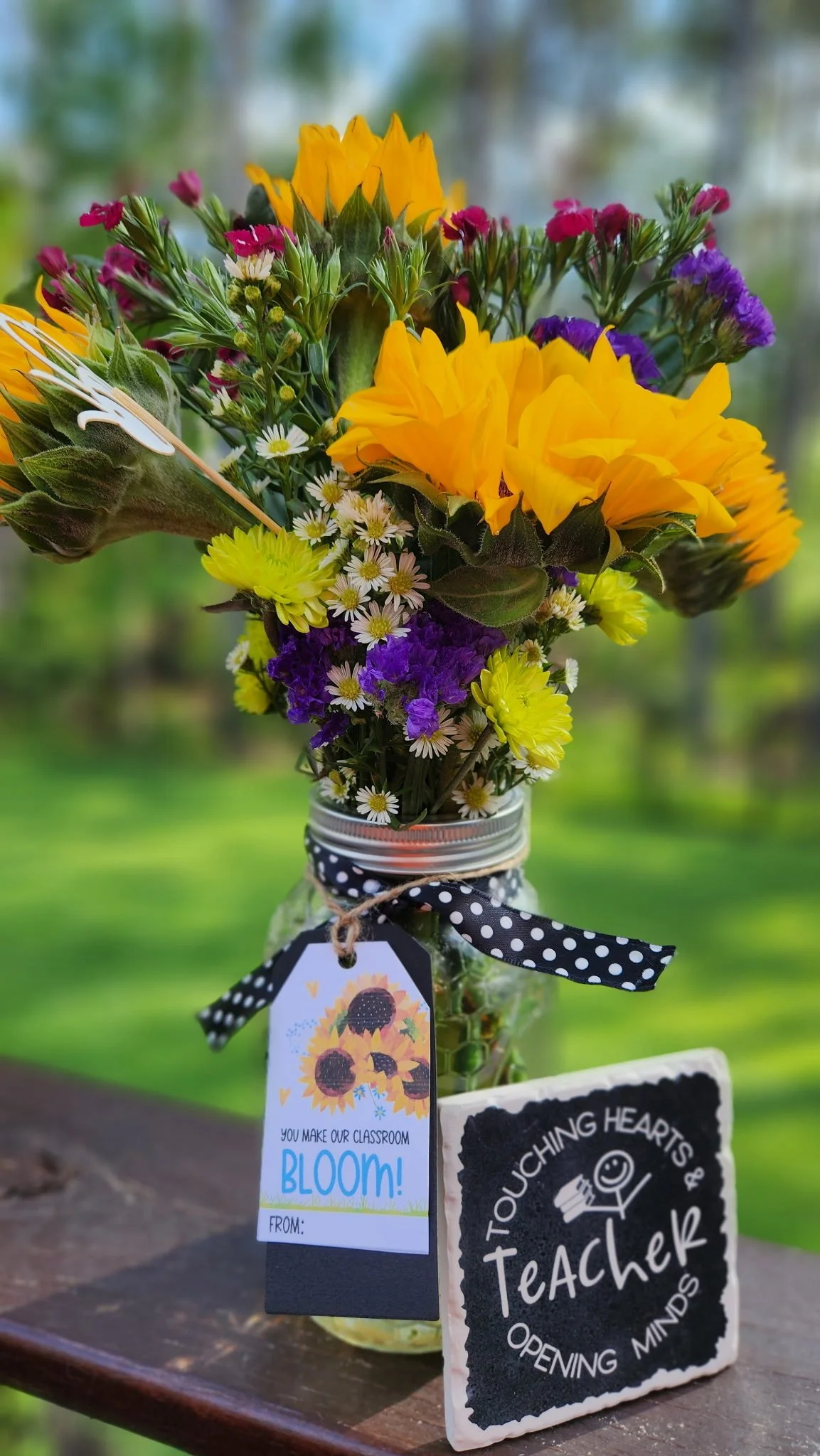 Colorful bouquet of flowers in a jar with a tag that says 'You make our classroom bloom!' and a sign that reads 'Touching hearts & opening minds Teacher'