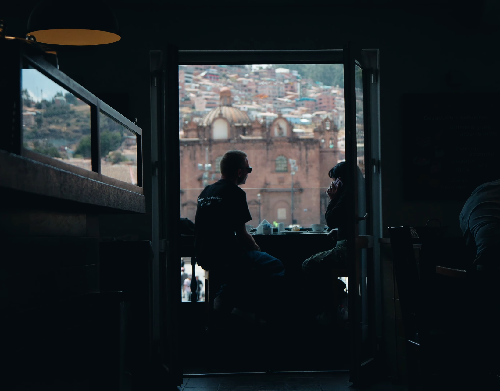 Silhouetted people sitting by a window overlooking a cityscape.
