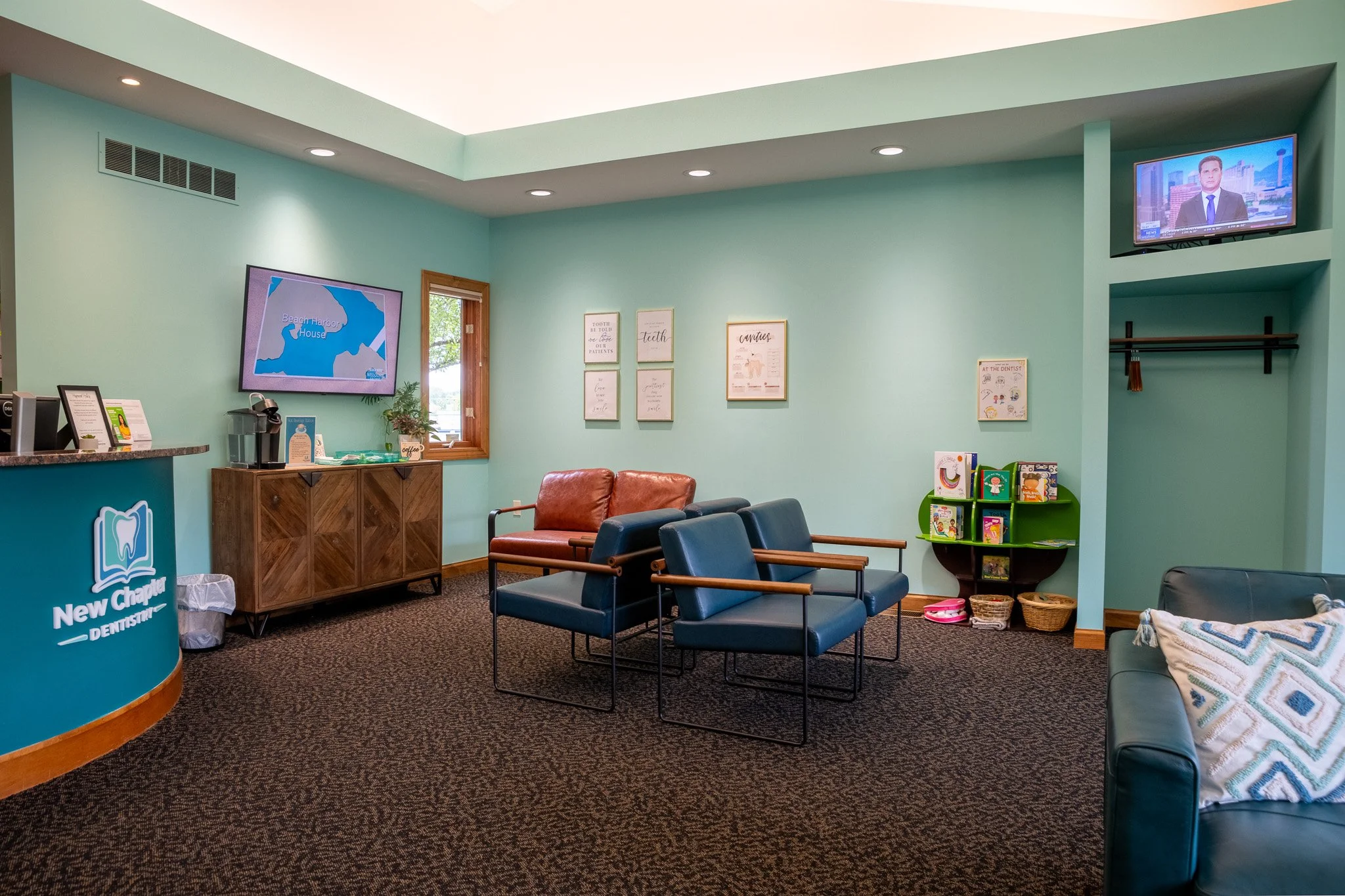 New Chapter Dentistry's waiting room with blue chairs, a leather couch, a green bookshelf with children's books, and a mounted TV showing news, all in a mint green room.