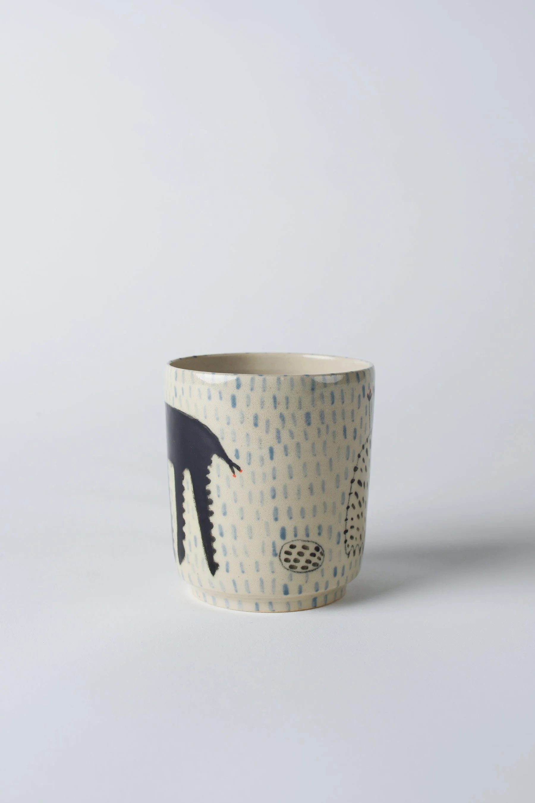 Ko-hi-Tasse aus Keramik mit schwarzem Wesen und langen Beinen – leicht gedrehte Ansicht zur Darstellung des Motivs.