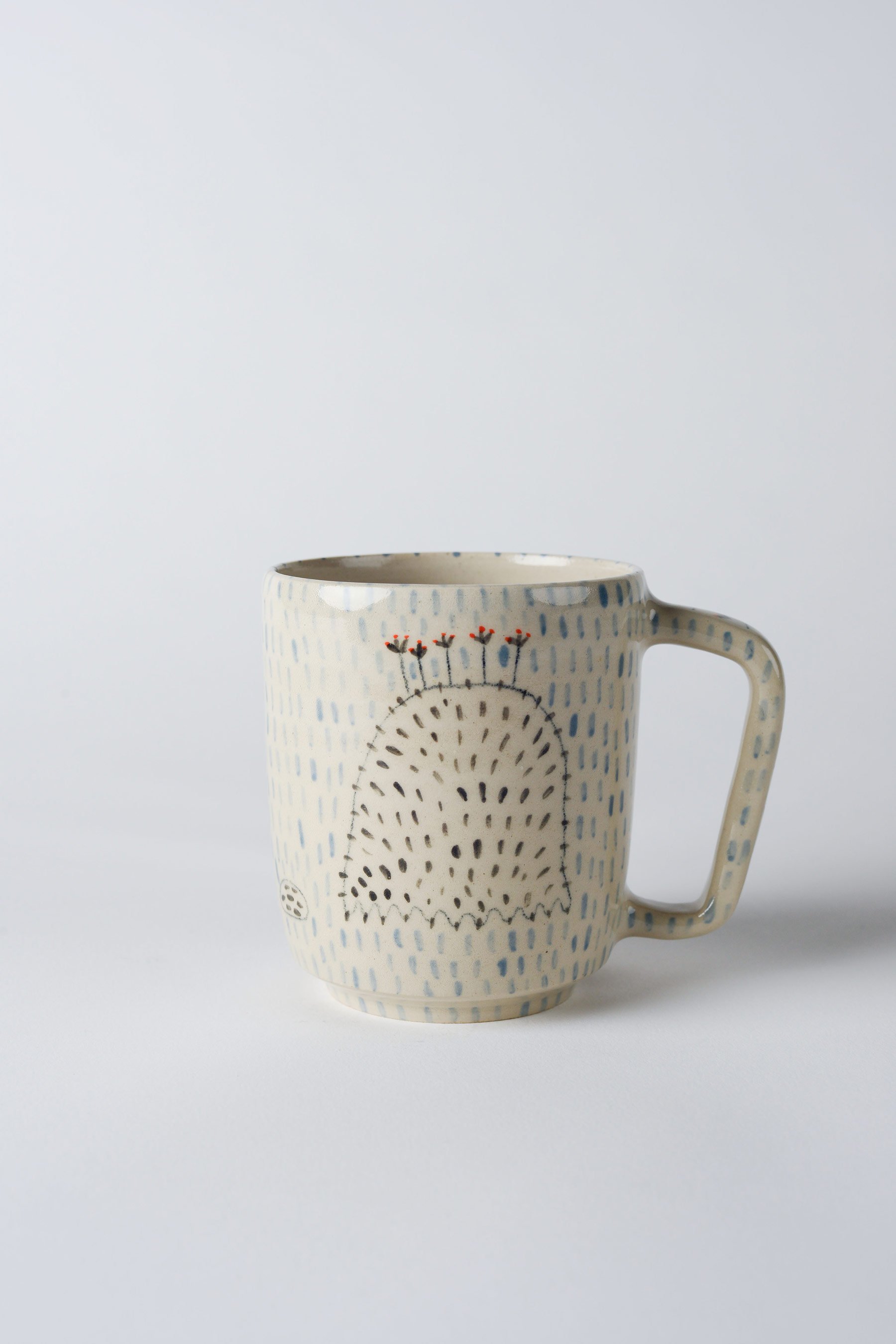 Ko-hi-Tasse aus Keramik mit dem gezeichneten schwarzen Wesen – weitere Drehansicht, um das umlaufende Motiv sichtbar zu machen.