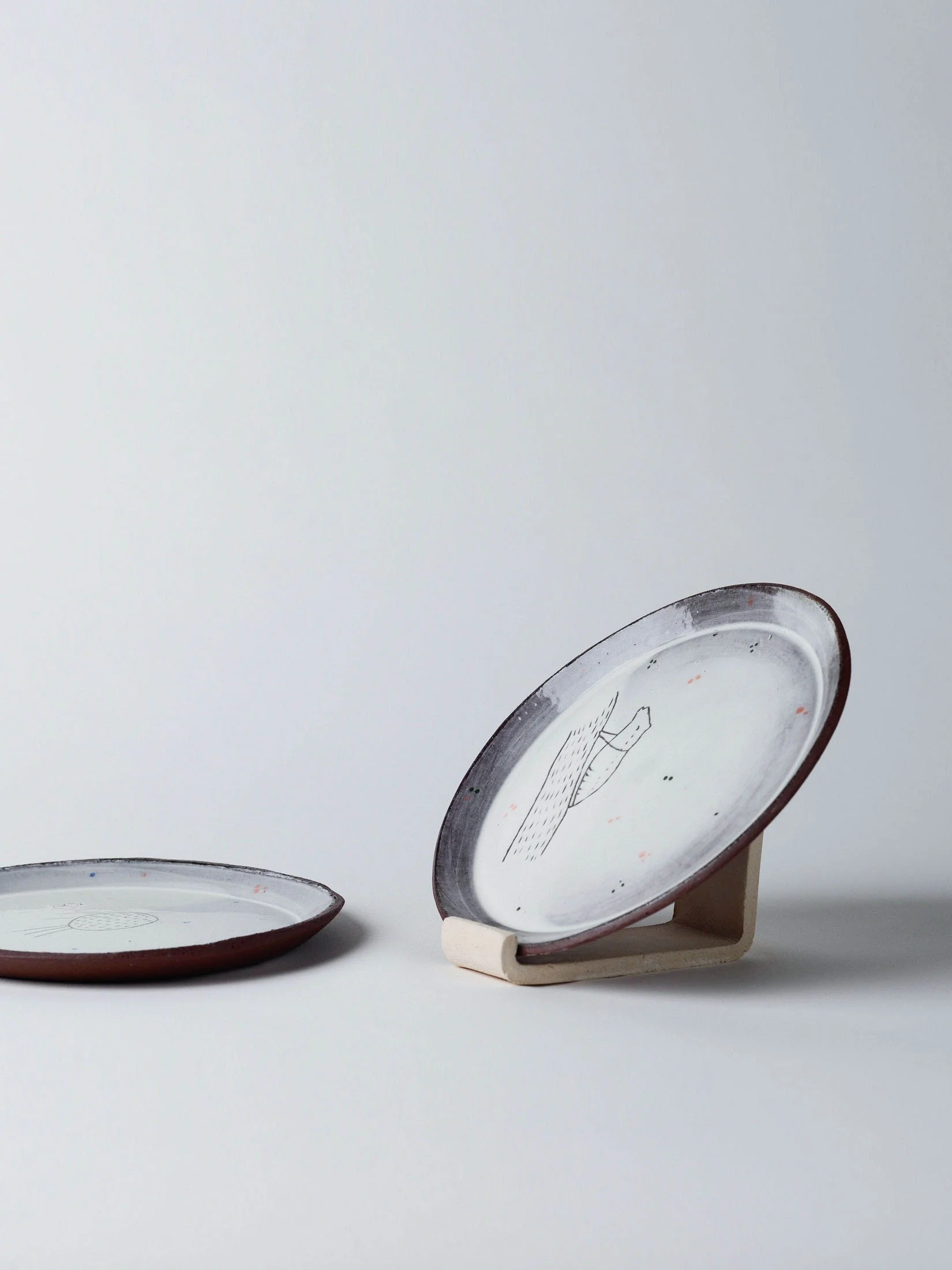 Seitliche Ansicht eines mittelgrossen Tellers mit sgraffito-Cocoon am Ast, zusammen mit weiteren handgefertigten Tellern aus dem Atelier KOBO