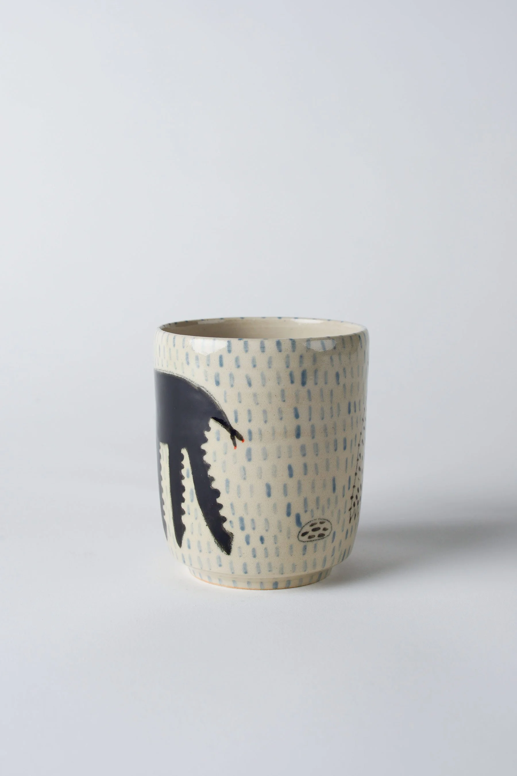 Ko-hi-Tasse aus Keramik mit schwarzem Wesen und langen Beinen – leicht gedrehte Ansicht zur Darstellung des Motivs.