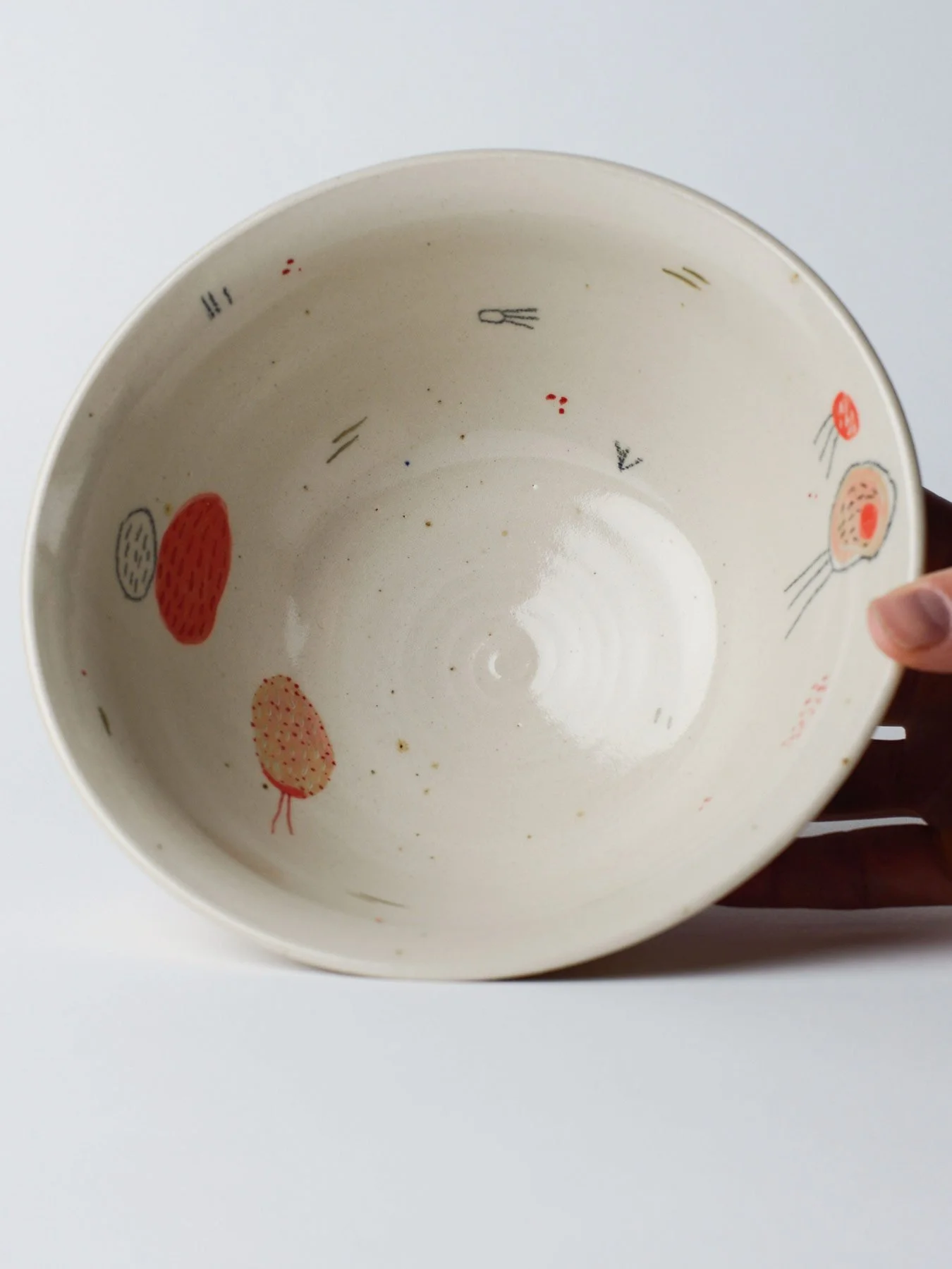 Udon-Schale mit kleinen gezeichneten Wesen – in der Hand gekippt, zeigt die innen glasierten Flächen.