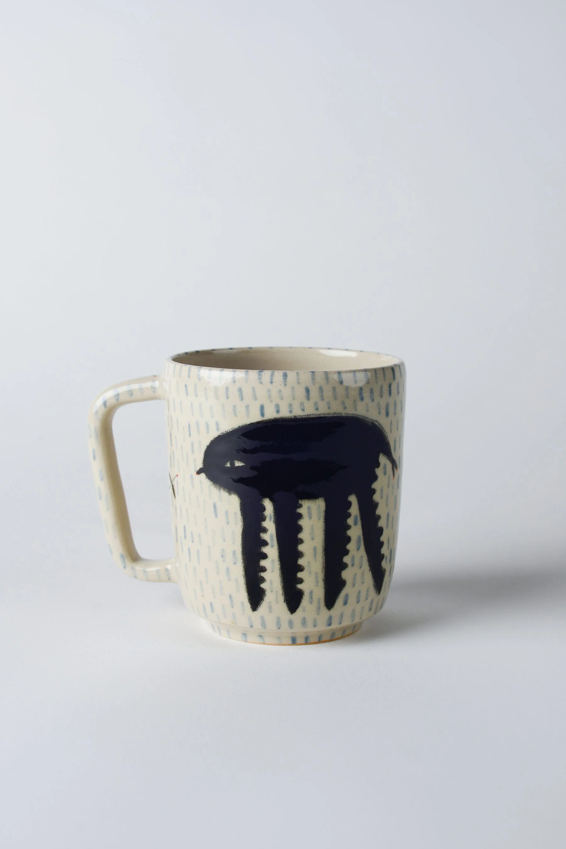 Ko-hi-Tasse aus Keramik mit gezeichnetem schwarzen Wesen und langen Beinen – vollständige frontale Ansicht.
