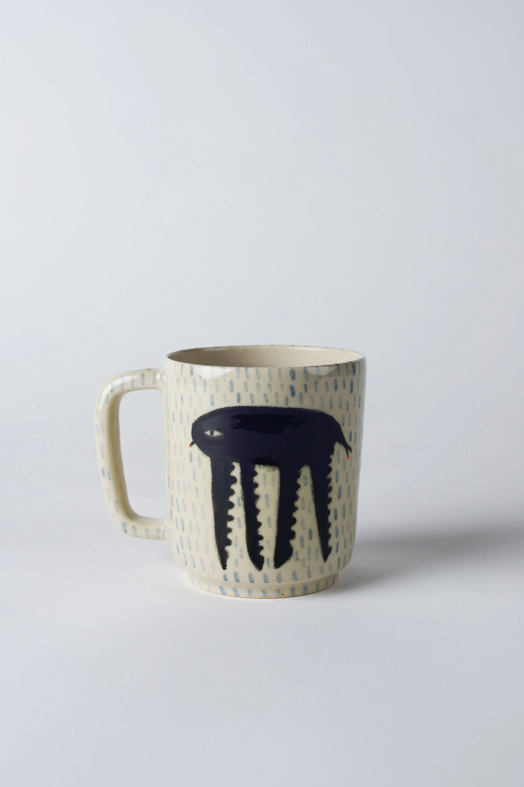 Ko-hi-Tasse aus Keramik mit gezeichnetem schwarzen Wesen und langen Beinen – vollständige frontale Ansicht.