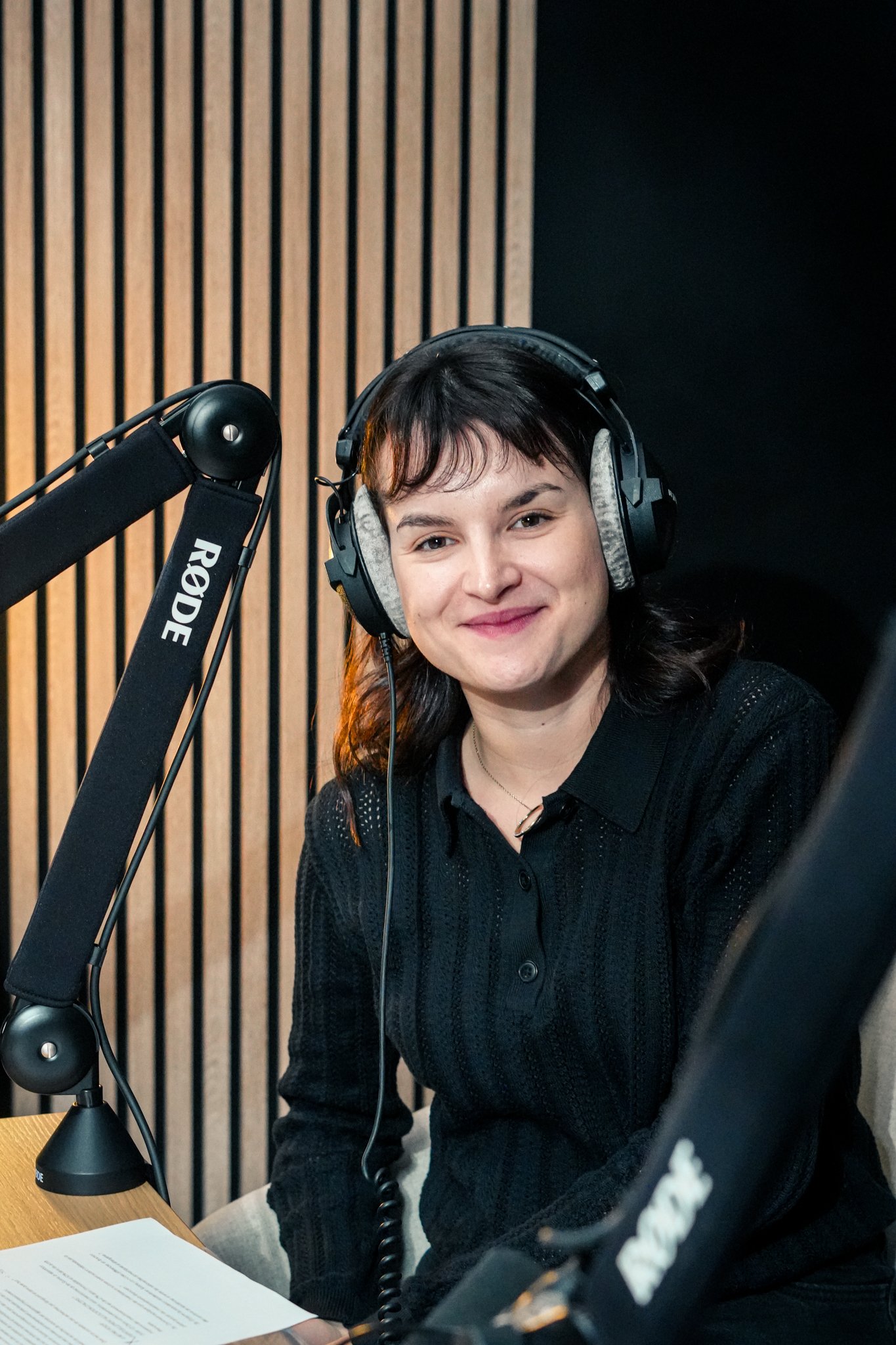 Une femme souriante portant un casque d'écoute dans un studio d'enregistrement avec un microphone Rode.