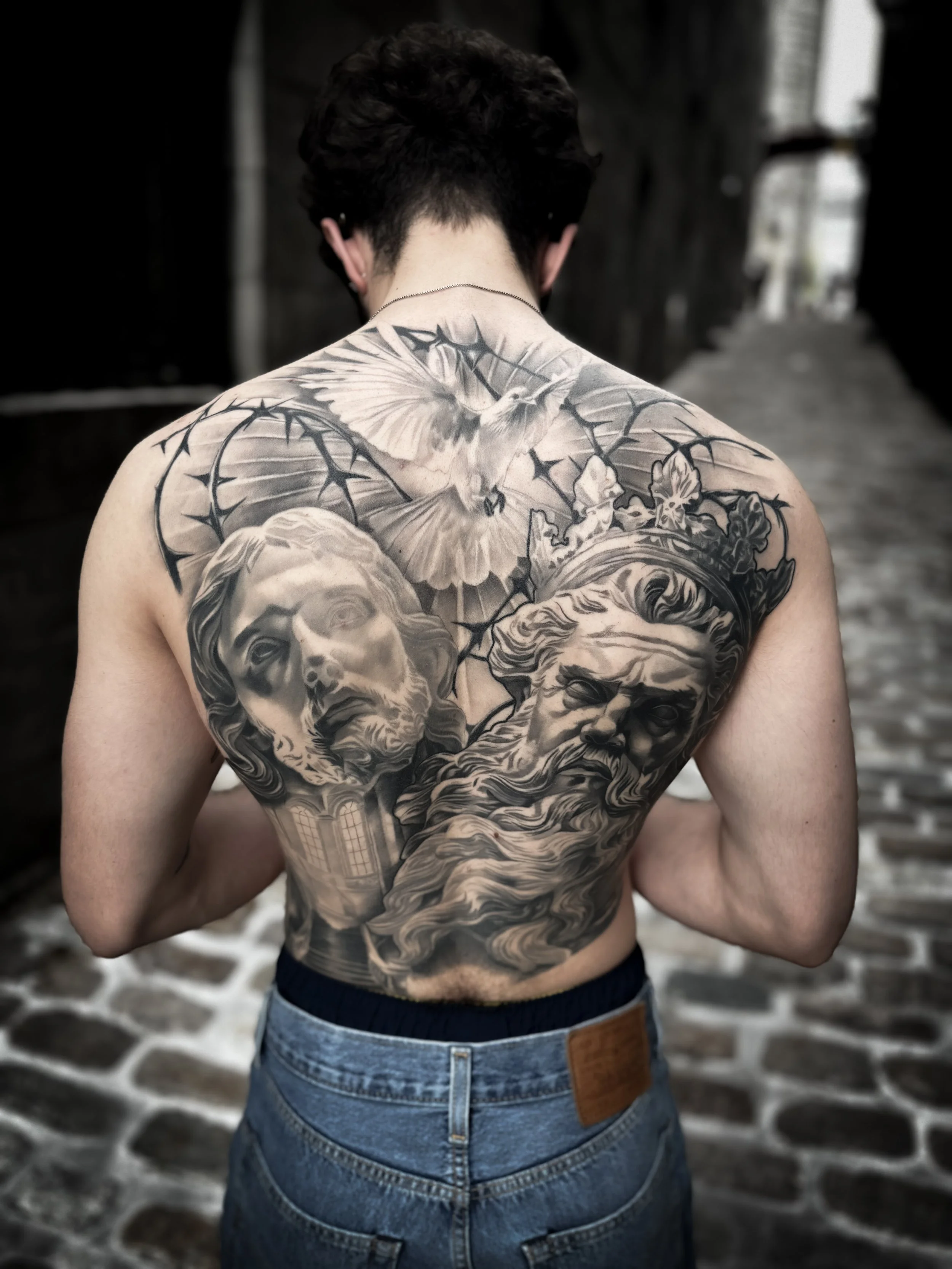 Dos complet réalisé en black & grey réaliste. Composition épique mêlant iconographie religieuse et mythologique : Jésus, Zeus couronné, colombe symbolisant la paix et la foi, entourés d'une couronne d'épines. darick tattoos