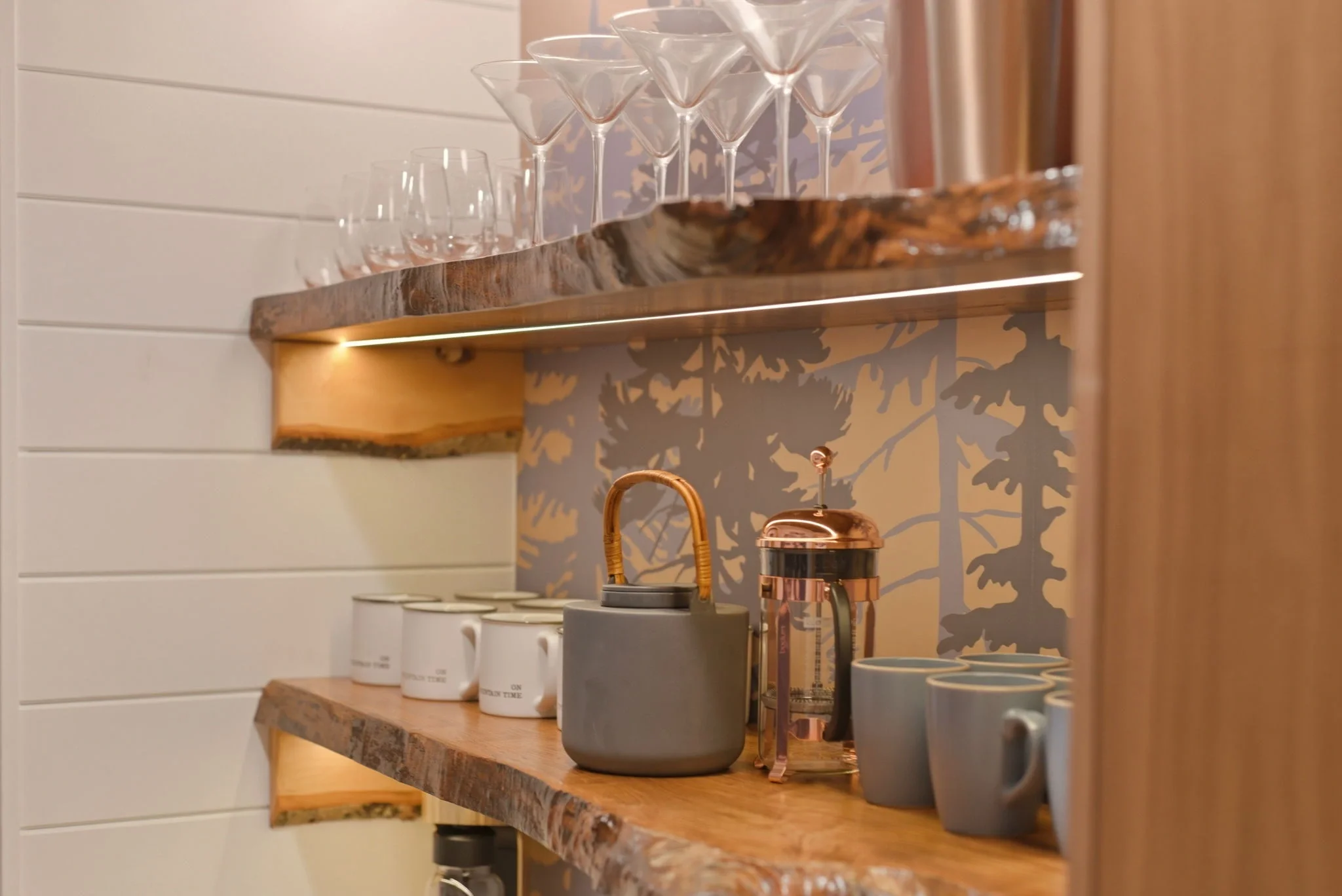 Live-edge maple shelf with teapot and mugs at Fjellsangin coffee bar, forest wallpaper