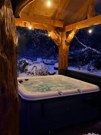 Covered hot tub in the cedar-post pavilion at night with snow on the ground at Fjellsangin in Ashford WA