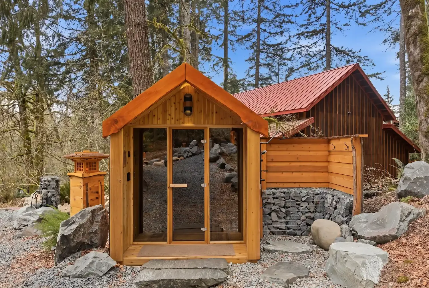 The private cedar sauna at Fjellsangin with a peaked roof and glass door, set among boulders in the Pacific Northwest forest in Ashford, Washington