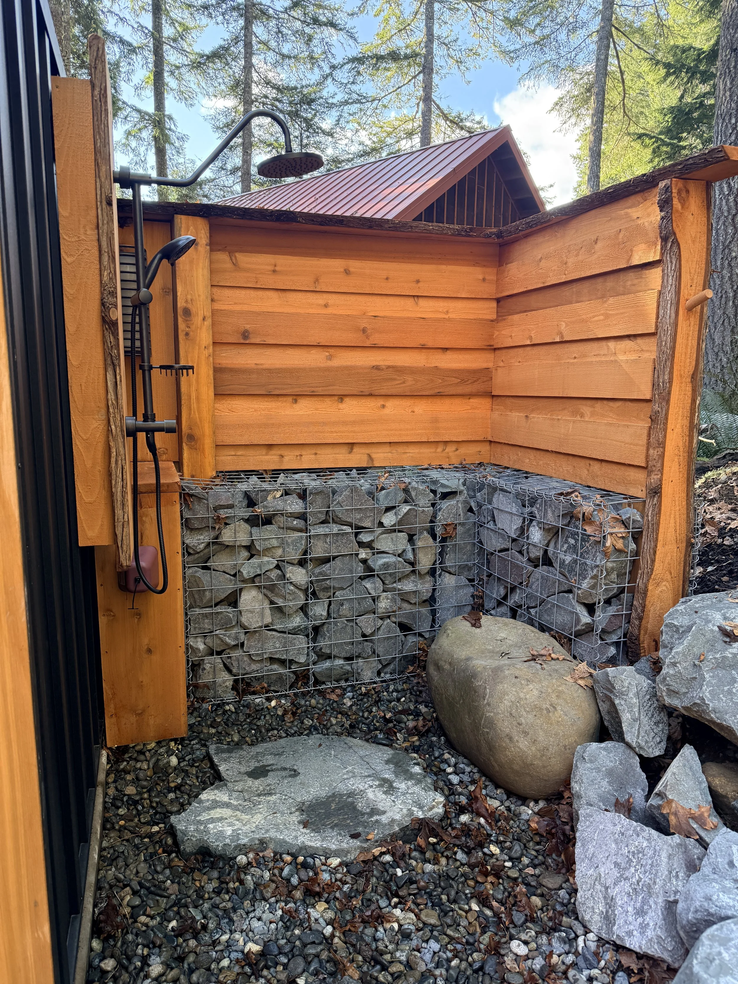 Outdoor shower with cedar walls, stacked stone and a glacial boulder seat at Fjellsangin