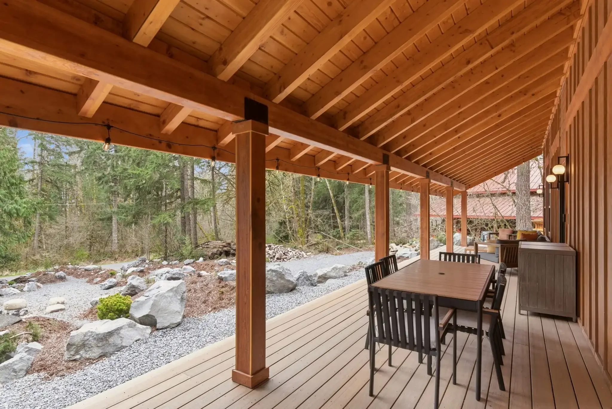 The covered cedar porch at Fjellsangin with an outdoor dining table, string lights, and an open view of the Japanese-Nordic garden in Ashford, Washington