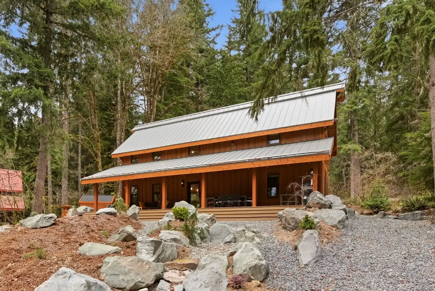 Fjellsangin cabin front exterior with wraparound porch and glacial boulders, Ashford, WA