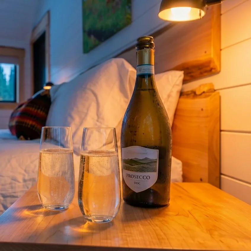 Fjellsangin Honeymoon Package arrival — chilled prosecco and two glasses on maple nightstand, cedar headboard and sconce glow