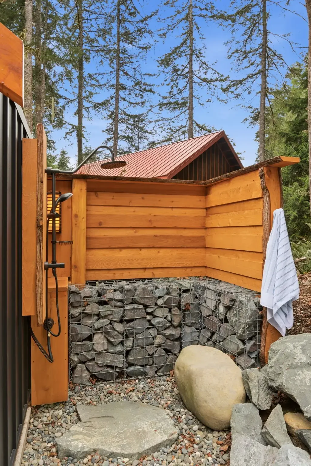 Outdoor shower with gabion rock wall and forest at Fjellsangin cabin near Mount Rainier