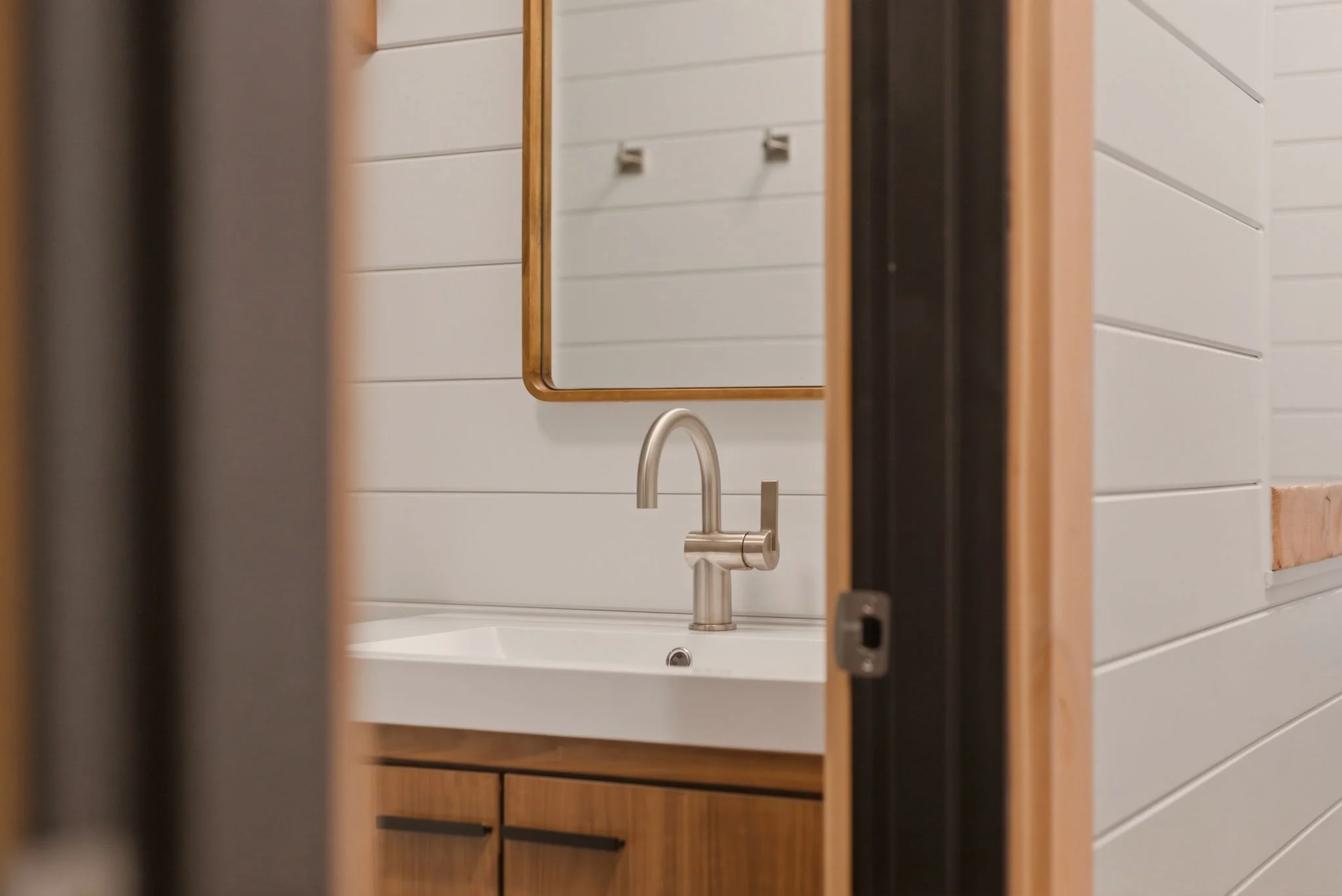 Bathroom vanity with brass-framed mirror and walnut cabinetry seen through pocket door at Fjellsangin cabin near Mount Rainier