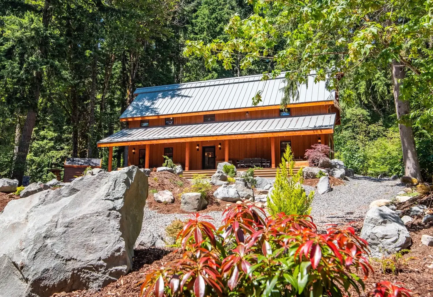 Fjellsangin cabin exterior with glacial boulder and rhododendron in bloom, forest cabin Ashford Washington