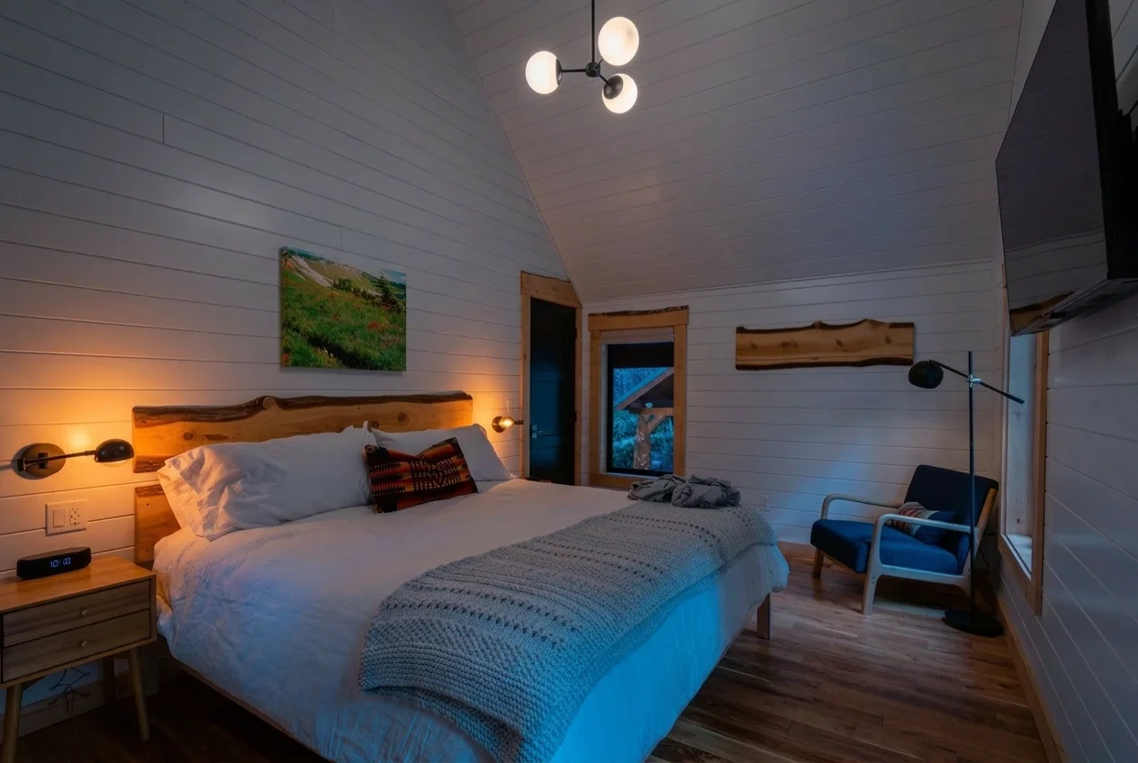 Fjellsangin honeymoon king bedroom at blue hour — cedar headboard, champagne flutes, sconce glow, forest view, Ashford WA