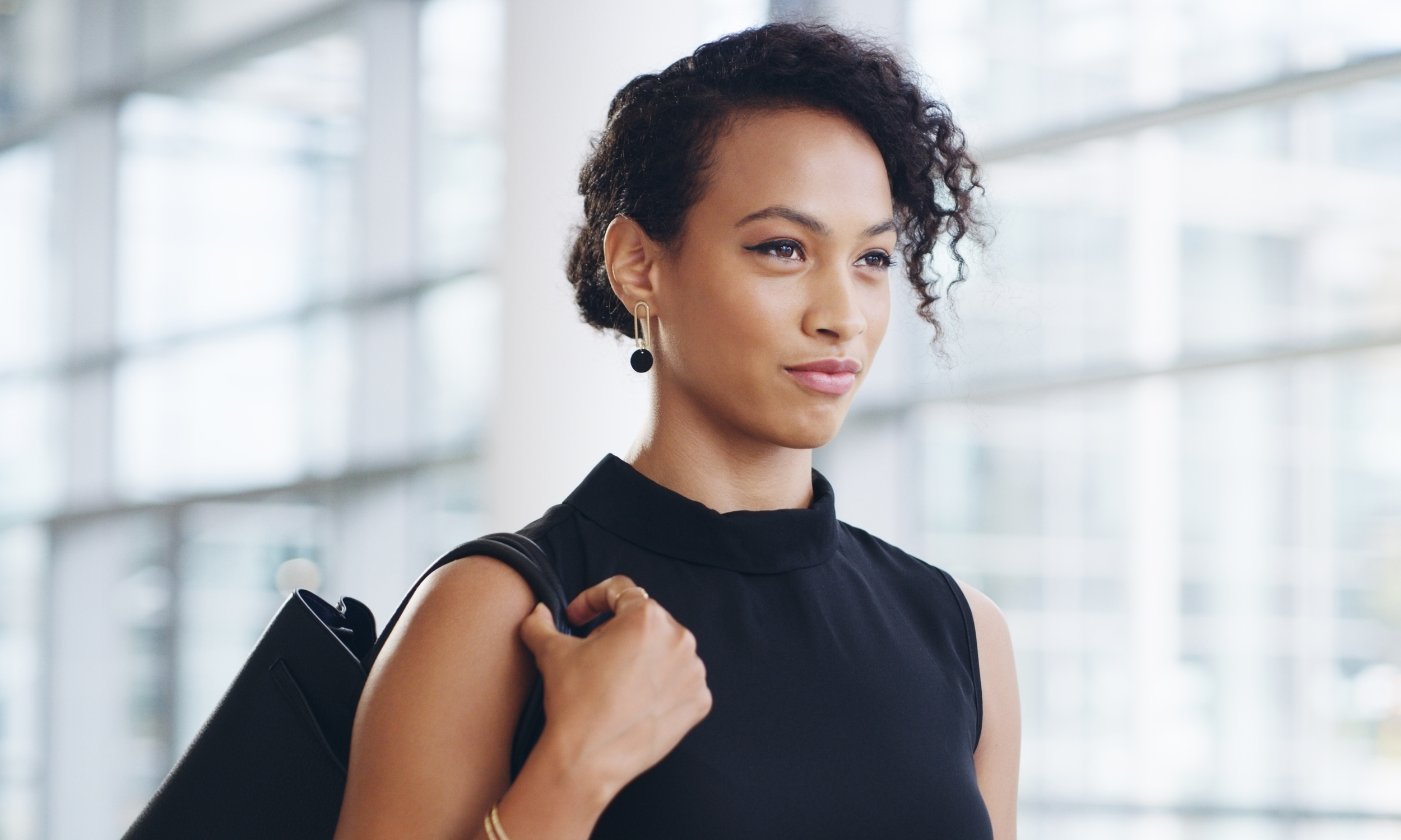 Black woman in professional clothing looking away pensively, symbolizing the emotional weight of high achievement and unspoken burnout.