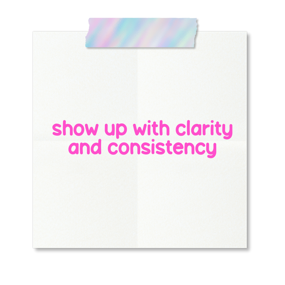 Pink text on a white paper note that says "show up with clarity and consistency" taped to a black background with rainbow-colored washi tape.