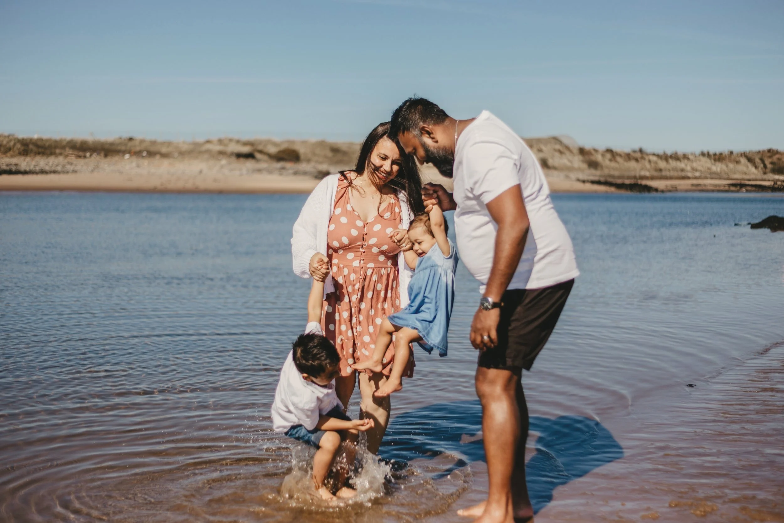 Family playing in shallow beach water on a sunny day.