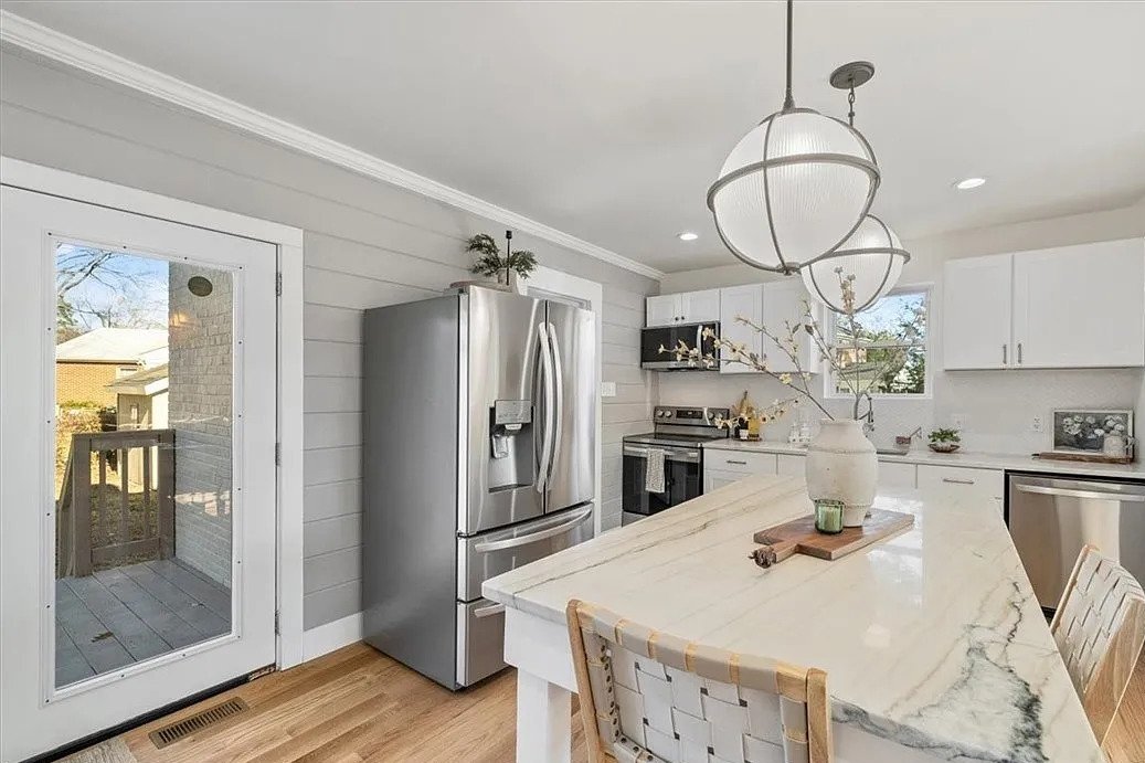 Modern kitchen with white cabinets, stainless steel refrigerator, and a marble countertop island decorated with a large vase and a small candle.