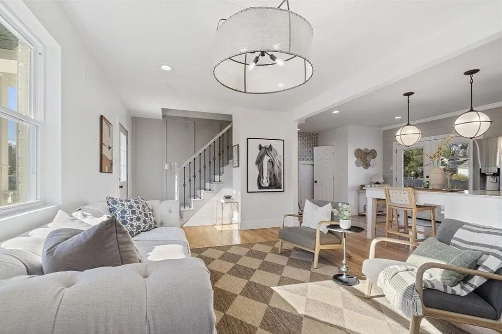 Living room with white walls, large windows, light-colored furniture, geometric area rug, and modern lighting fixtures.
