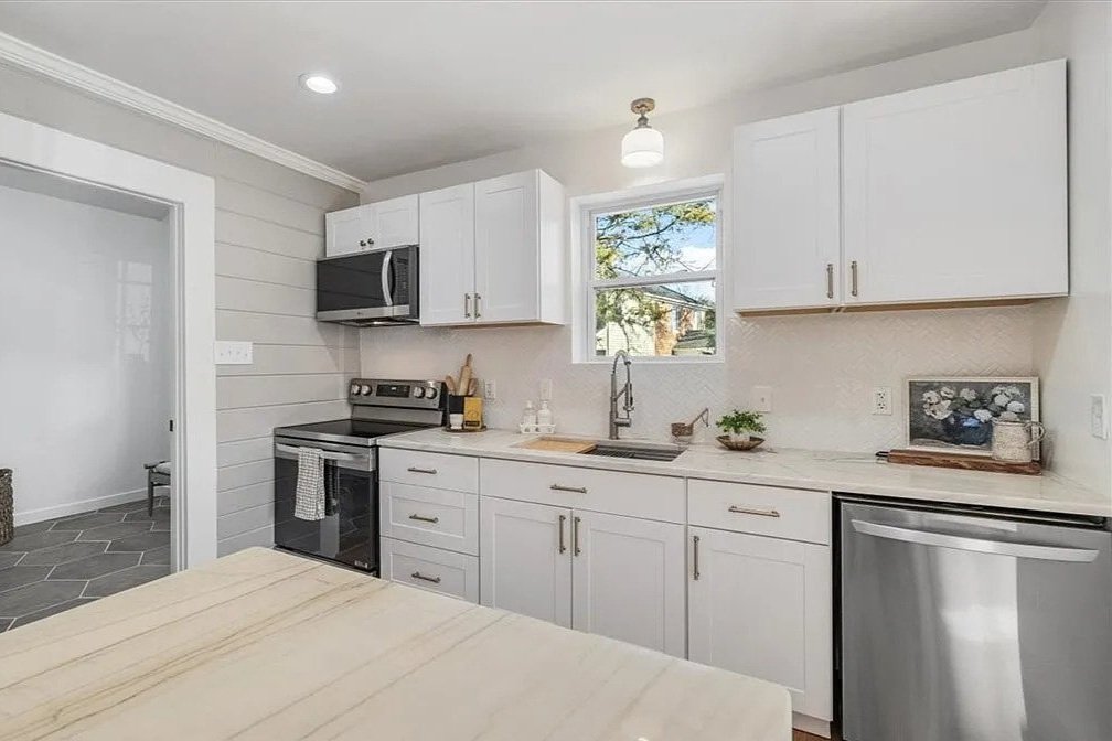 Clean kitchen with white cabinets, stainless steel appliances, and a window above the sink, featuring a beige countertop and minimal decor.