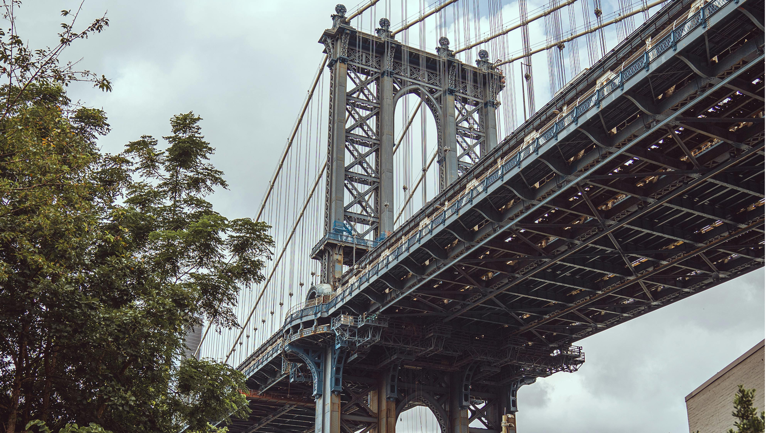 View of the Brooklyn Bridge in New York City with a cloudy sky in the background, showing the bridge's steel structure and suspension cables.