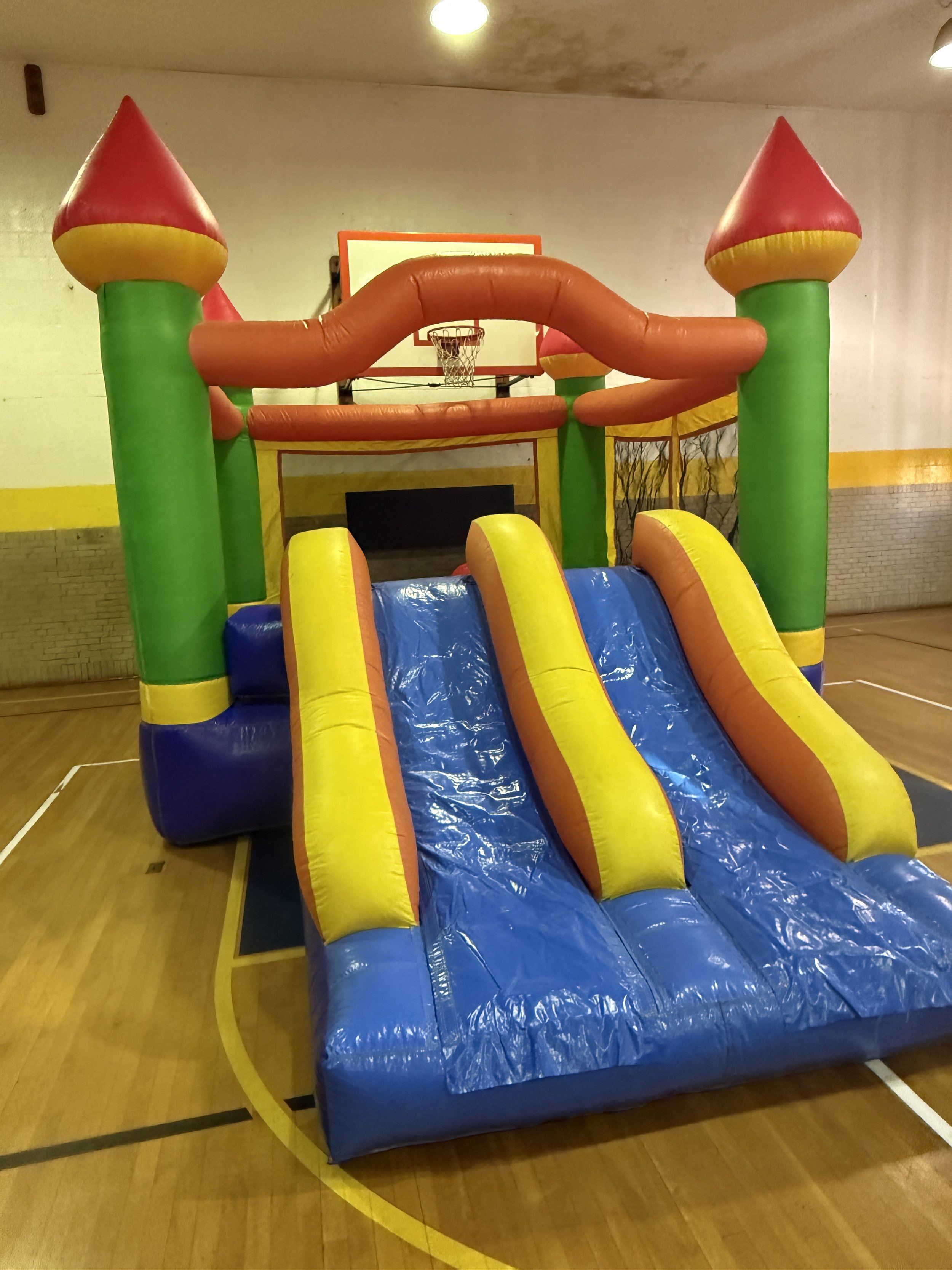 Colorful inflatable bounce house with two slides, designed for children, set up in a gymnasium.