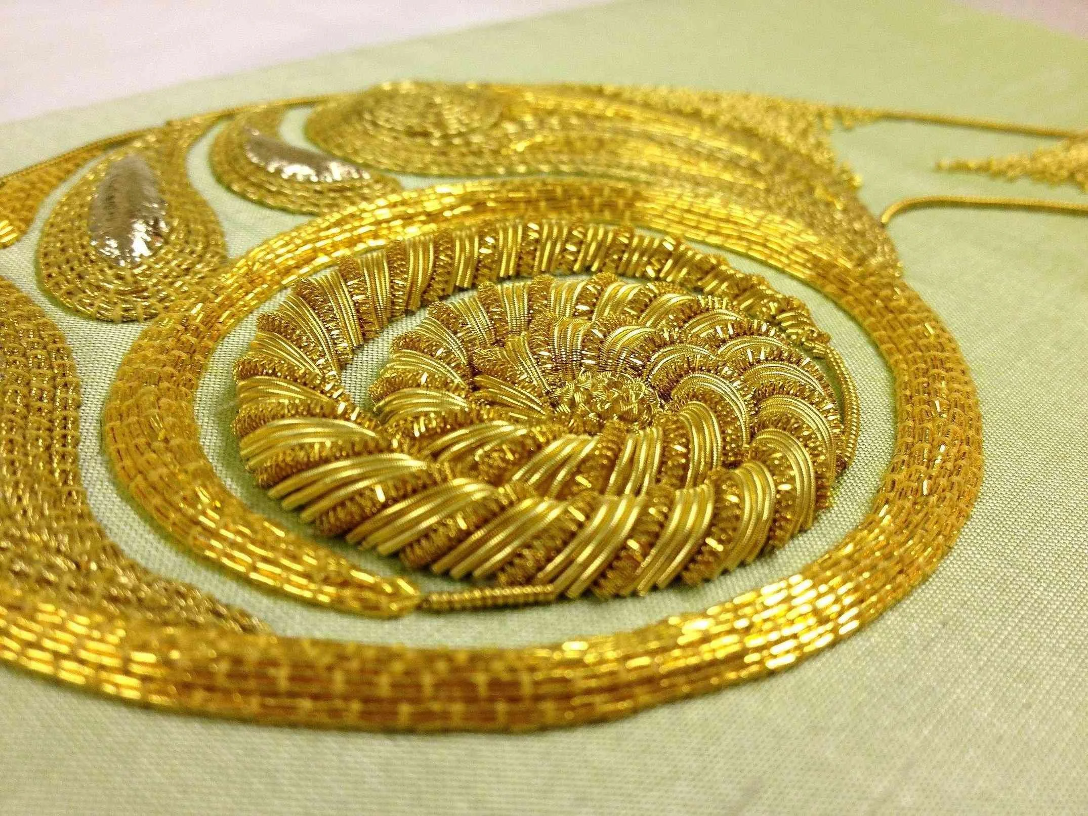 Close-up of a gold jewelry set on a light-colored fabric, including a necklace and a brooch with intricate, shiny designs.