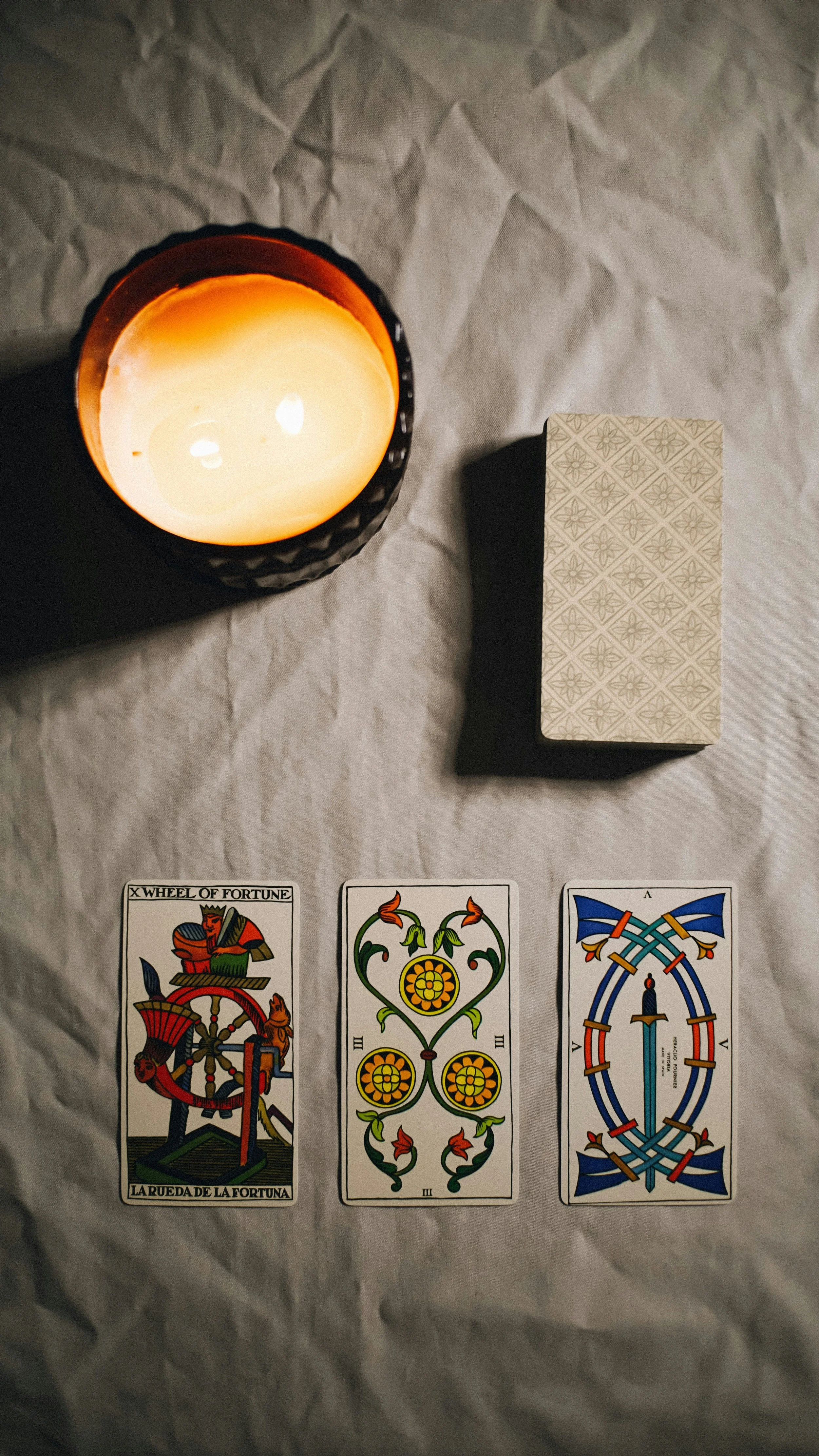 A lit candle in a black container, a deck of tarot cards, and three tarot cards laid out on a white surface for Felicity De Carlo Tarot reader and spiritual coach Melbourne