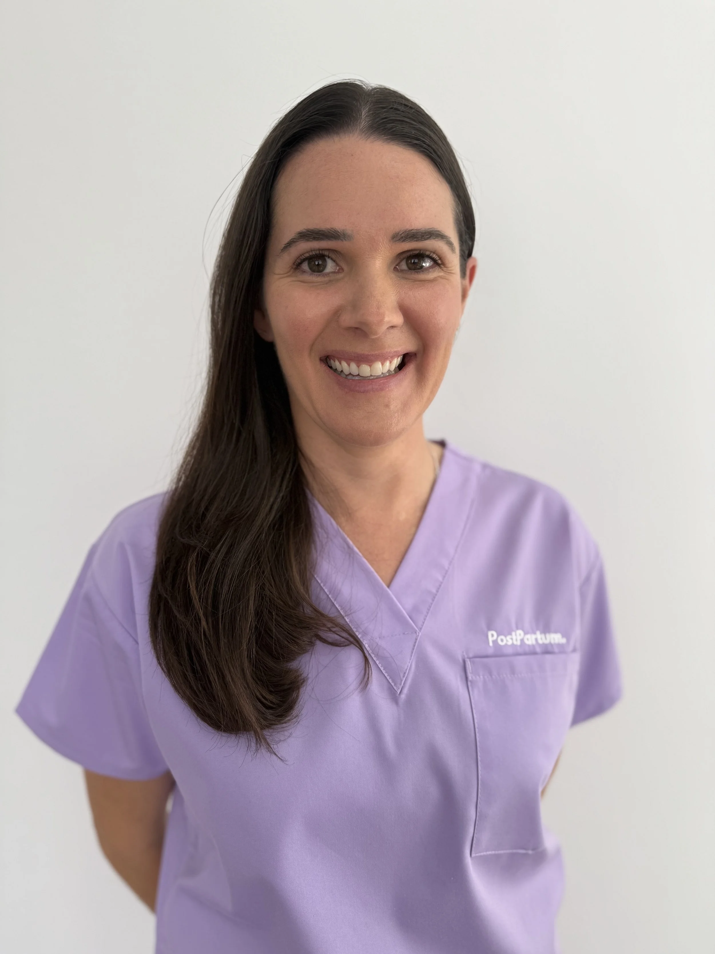 PostPartum midwife in purple scrubs smiling against a white background.
