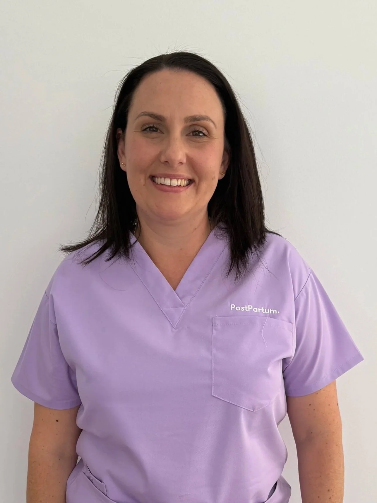 PostPartum midwife in purple scrubs smiling against a white background.
