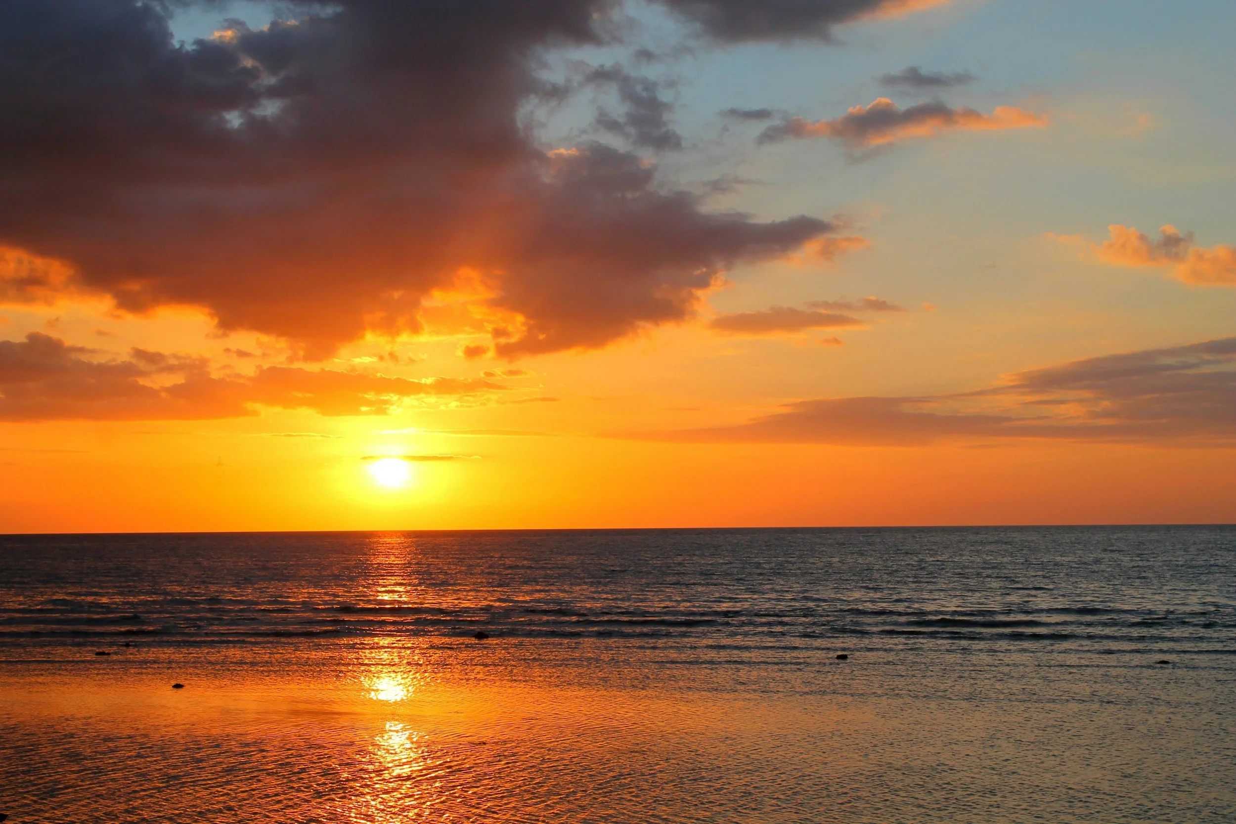 Sunset over the ocean with a partly cloudy sky, reflecting on the water's surface.