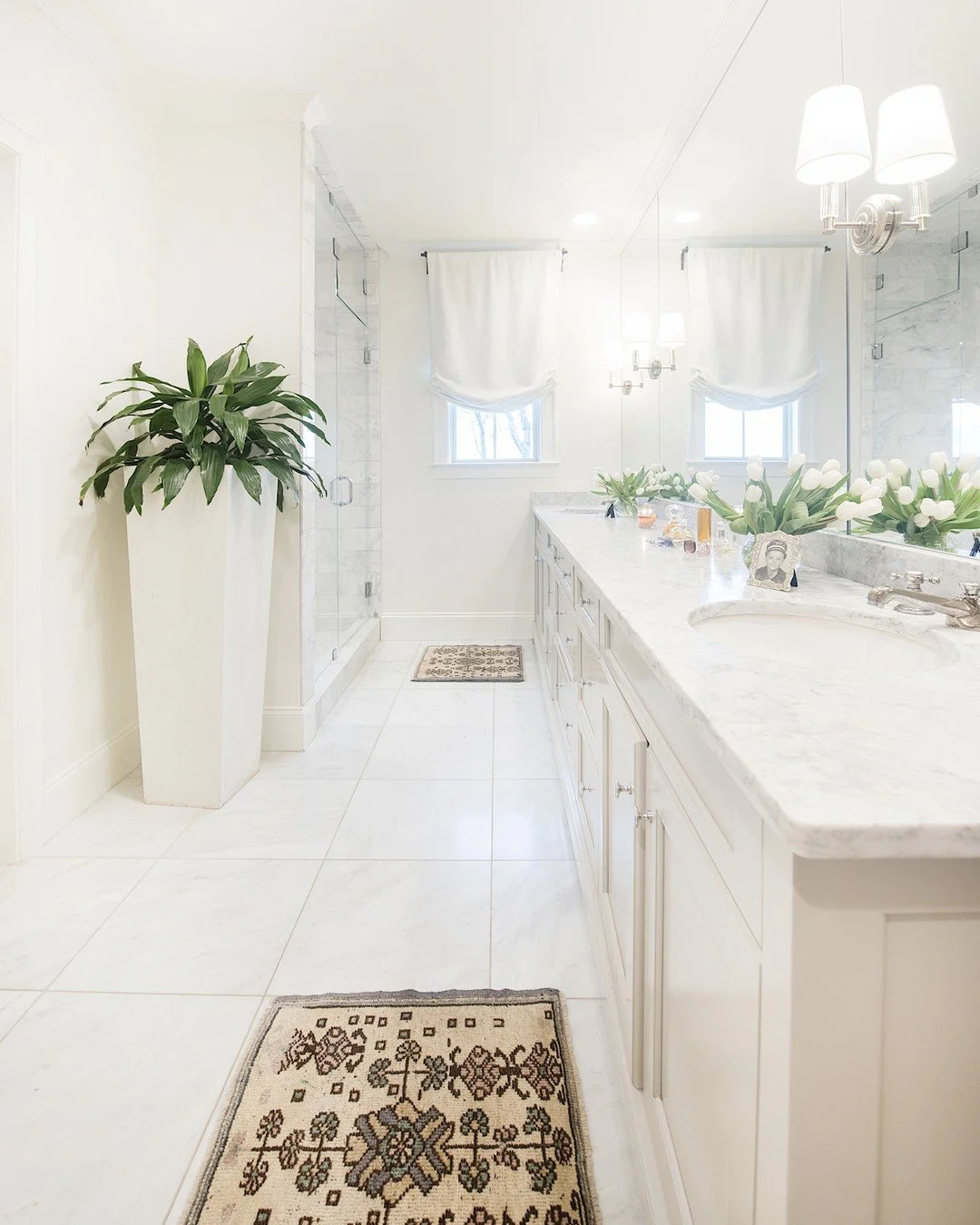 All white, all bright, all day. Marble countertops and a frameless glass shower keep this bathroom feeling light, while a statement planter and vintage rugs add just the right warmth. Fresh tulips and a few personal touches make it feel collected and